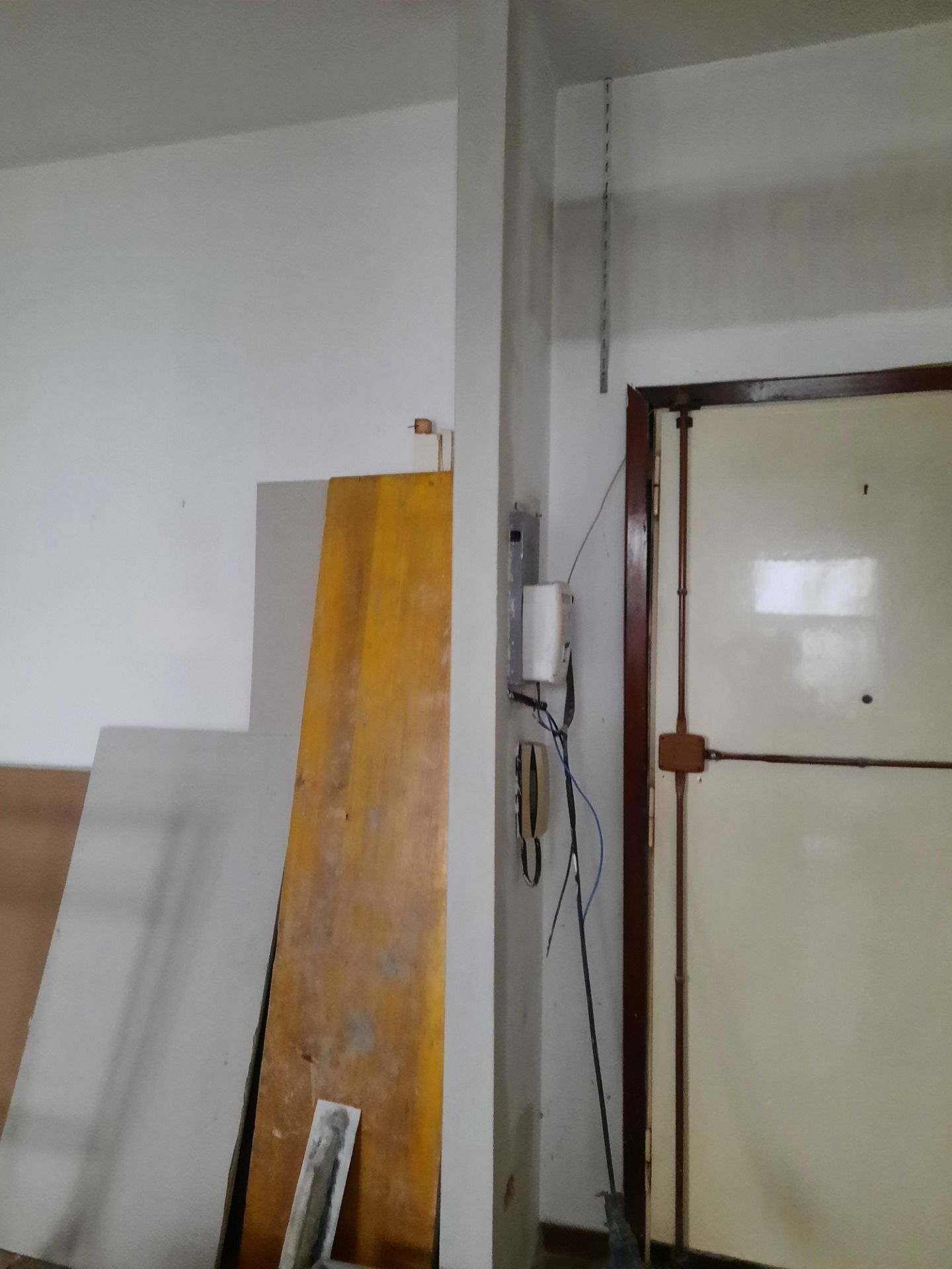 Vista interna: materiali da costruzione appoggiati a un muro accanto a una porta e a un quadro elettrico.