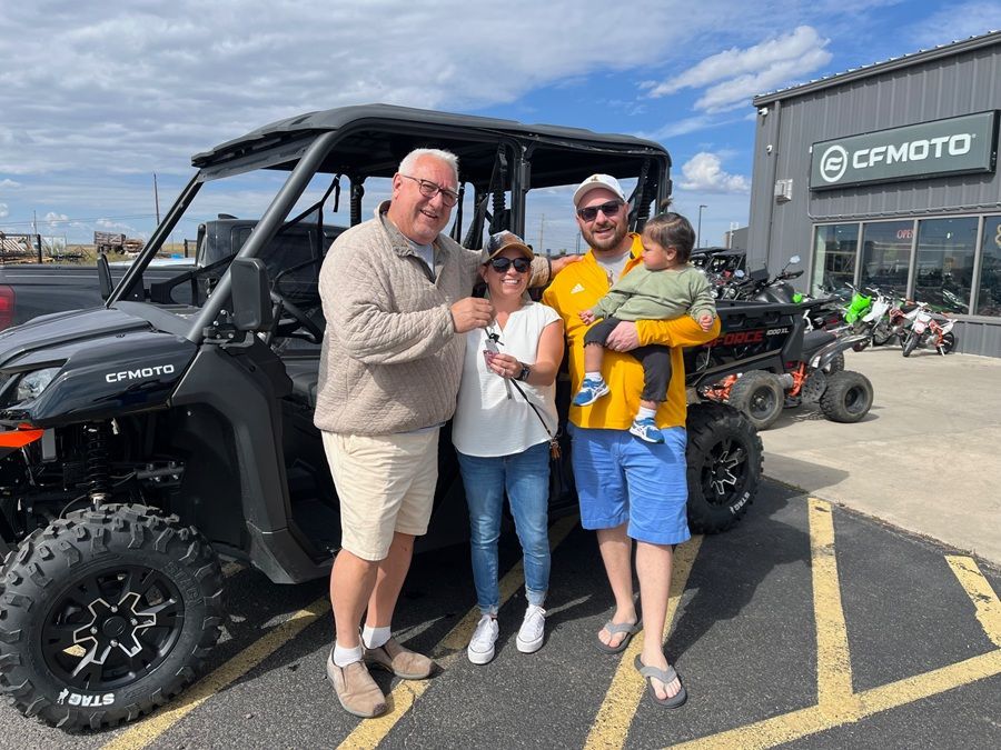 Family poses with new black CFMOTO UTV at dealership.