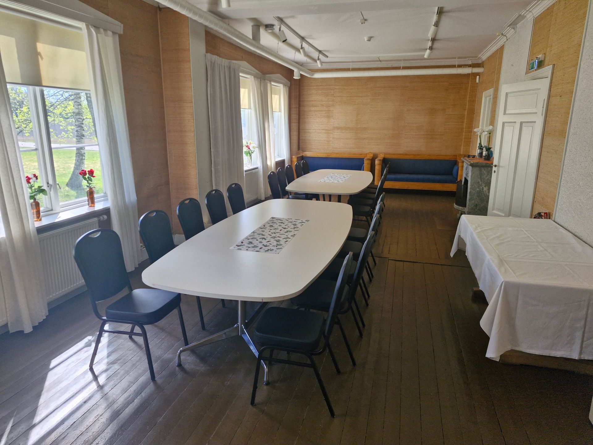 Konservatorboligen med lange bord, klappstoler og store vinduer ved siden av et tregulv.