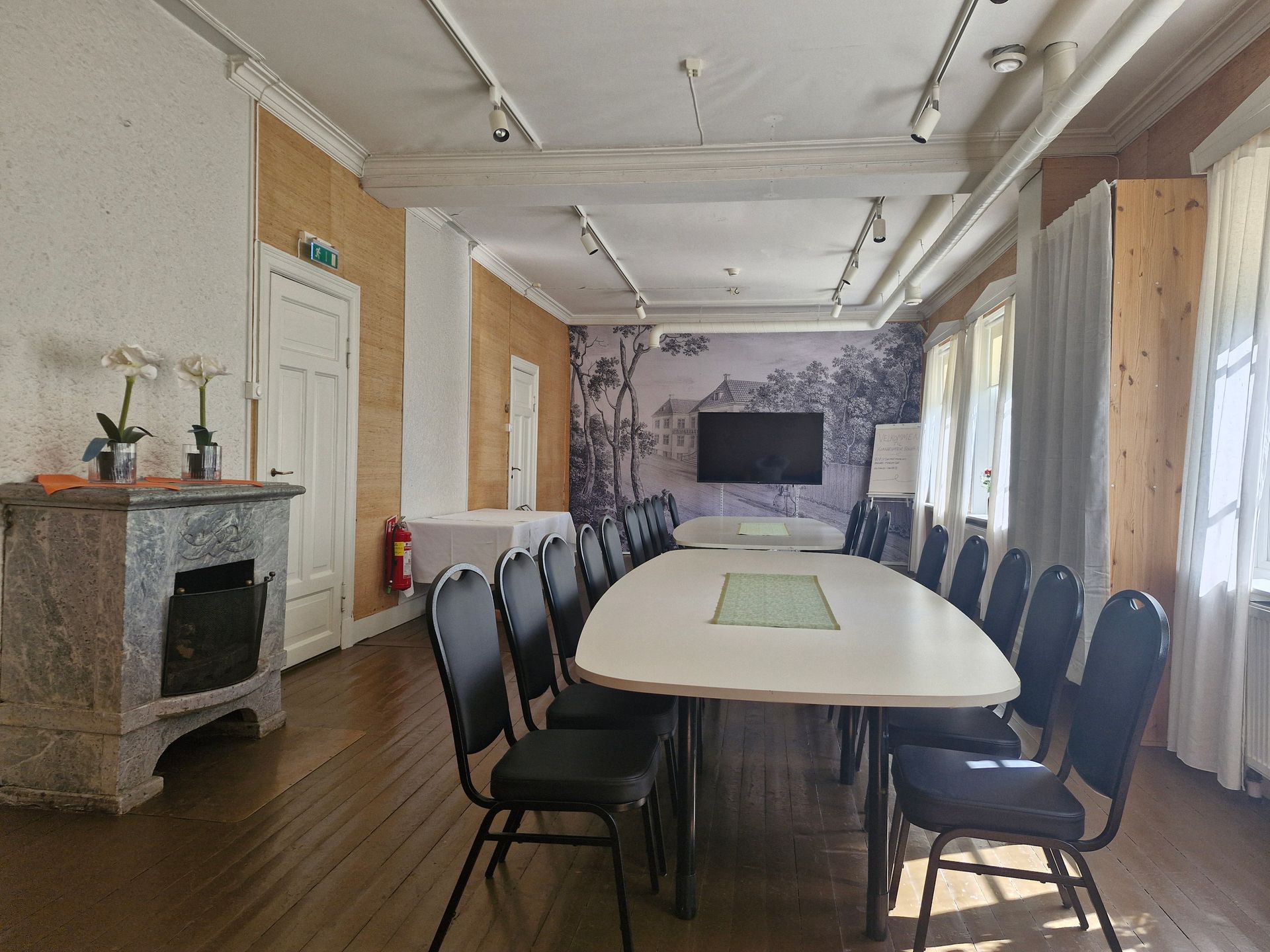 Langt konferanserom med et hvitt bord, svarte stoler, peis og veggmontert TV