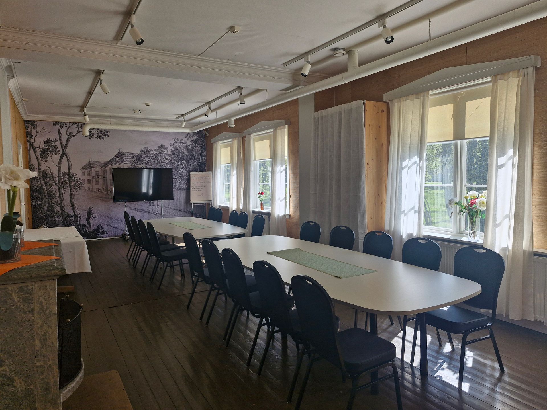Langt konferansebord med blå stoler i et lyst møterom med vinduer og gardiner