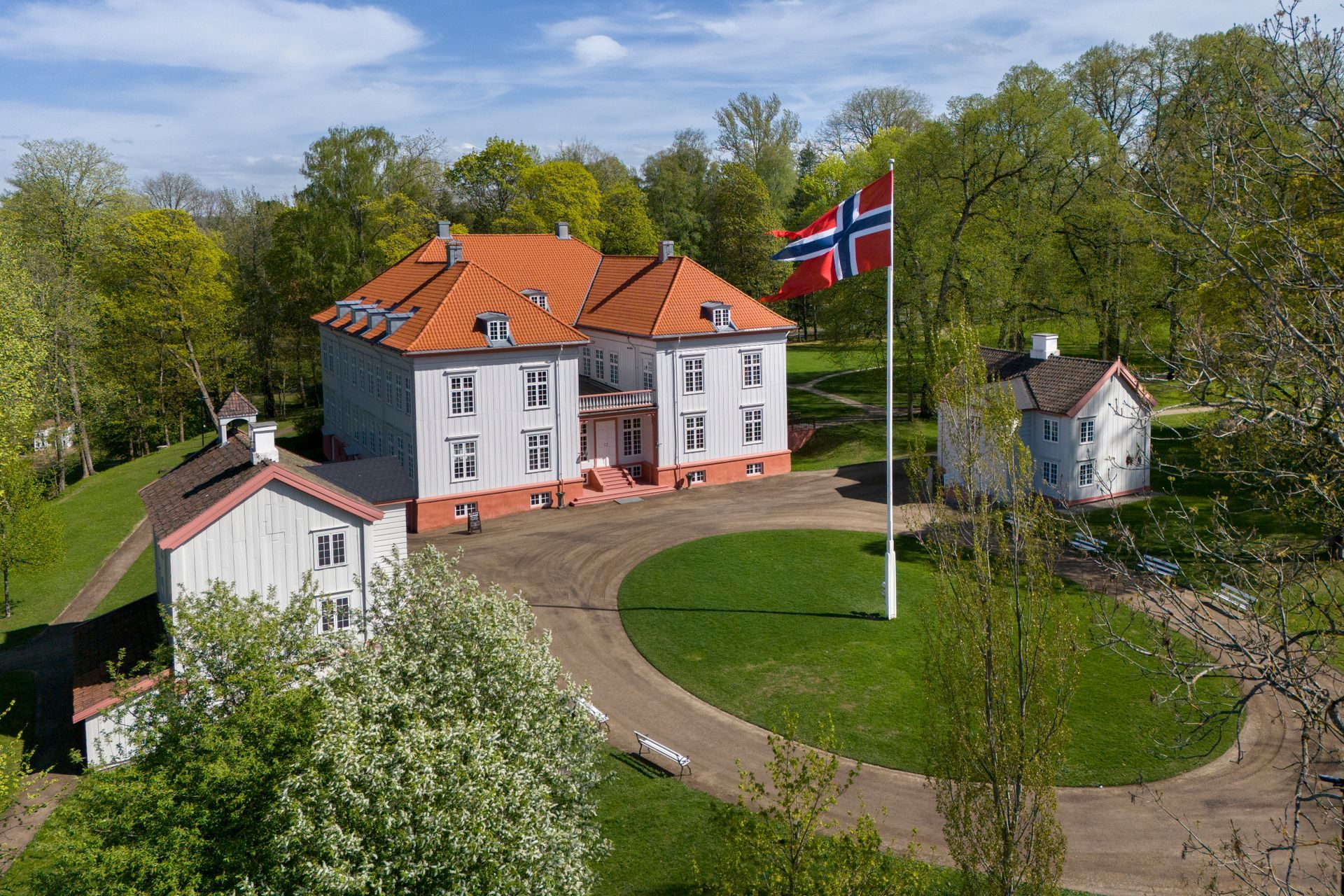 Blått hus med oransje tak, veranda og tilhørende garasje på en grønn plen, solrik dag.