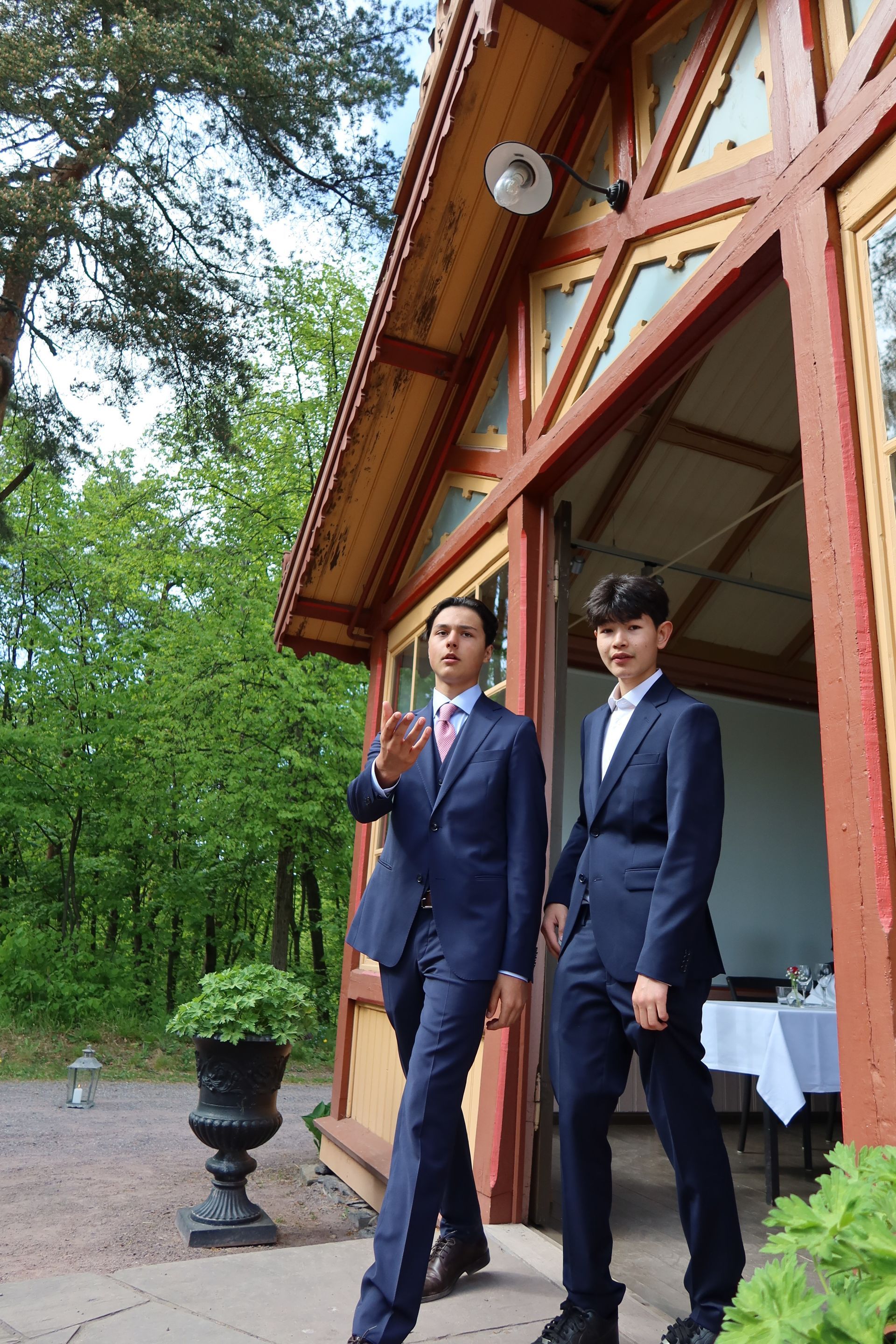 Kvinne i blomsterkjole, to menn i dress ved en døråpning. Mann i blå dressjakke med knapper. Kvinnen smiler.