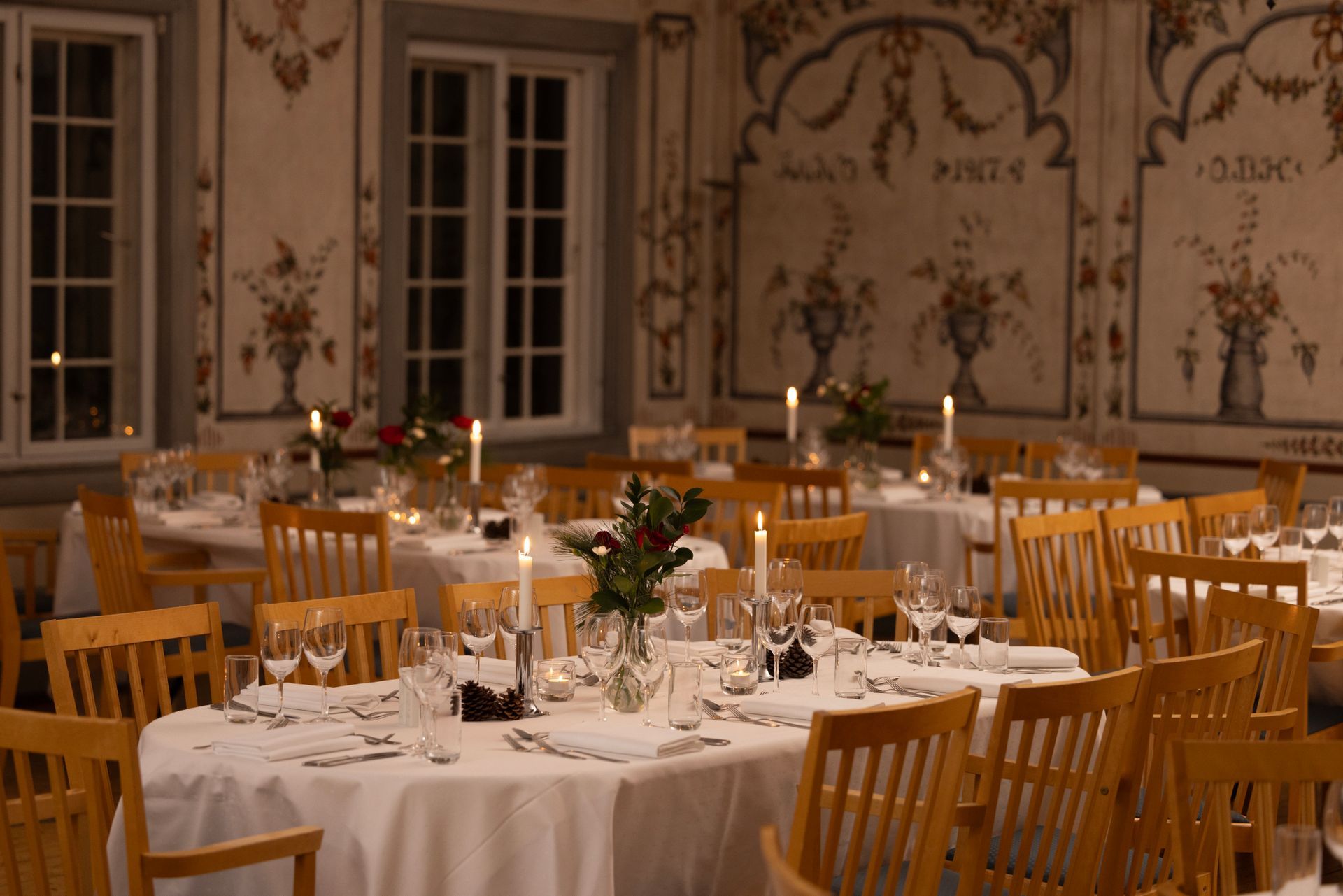 Langt spisebord dekket for et måltid i et rom med peis og vinduer.