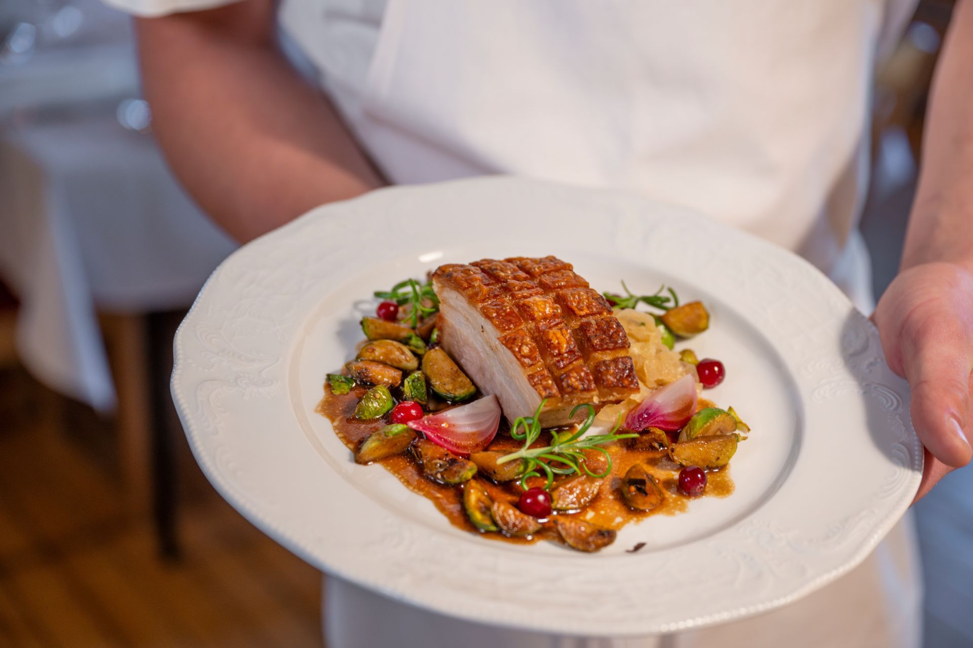 Kokk holder tallerken med stekt svinebuk med grønnsaker og saus.