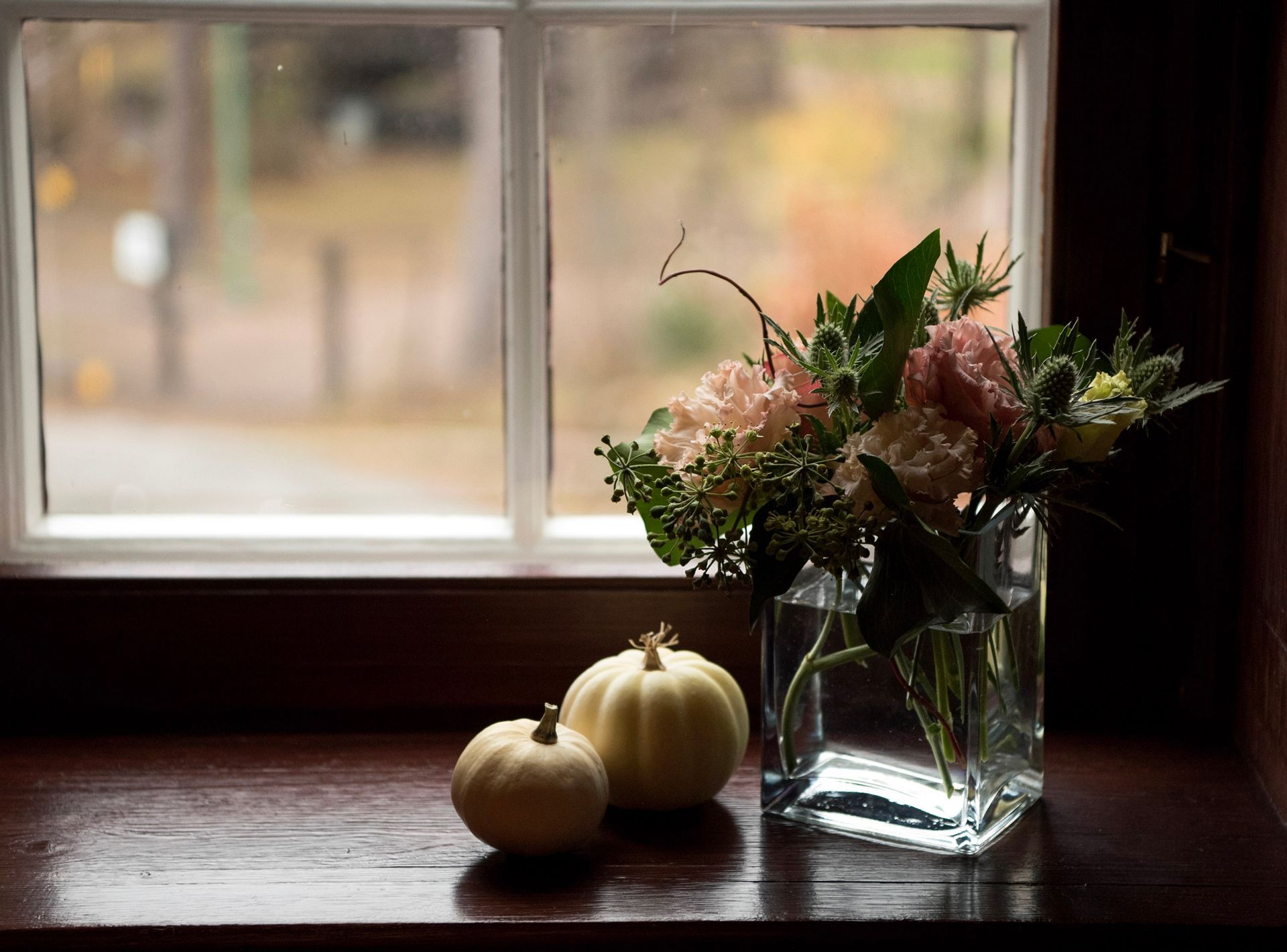 Vindu er pyntet med blomster og gresskar som skaper en koselig stemning i huset. 