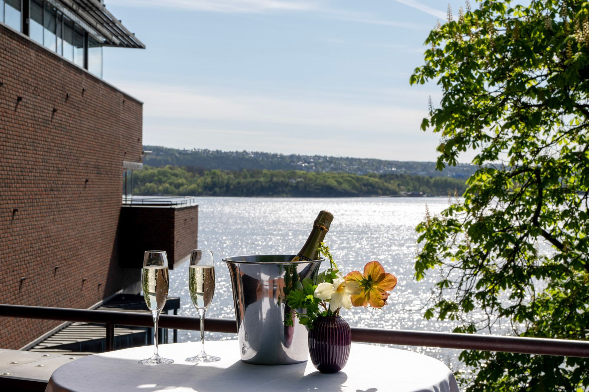 Champagneglass, bøtte med flaske, blomster og utsikt over Oslofjorden.