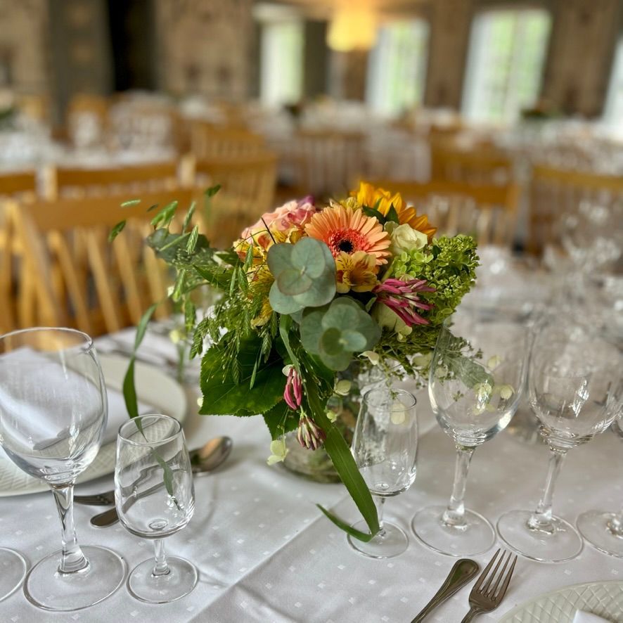 Borddekking med blomsterdekorasjon og glass, klart for et formelt arrangement innendørs.