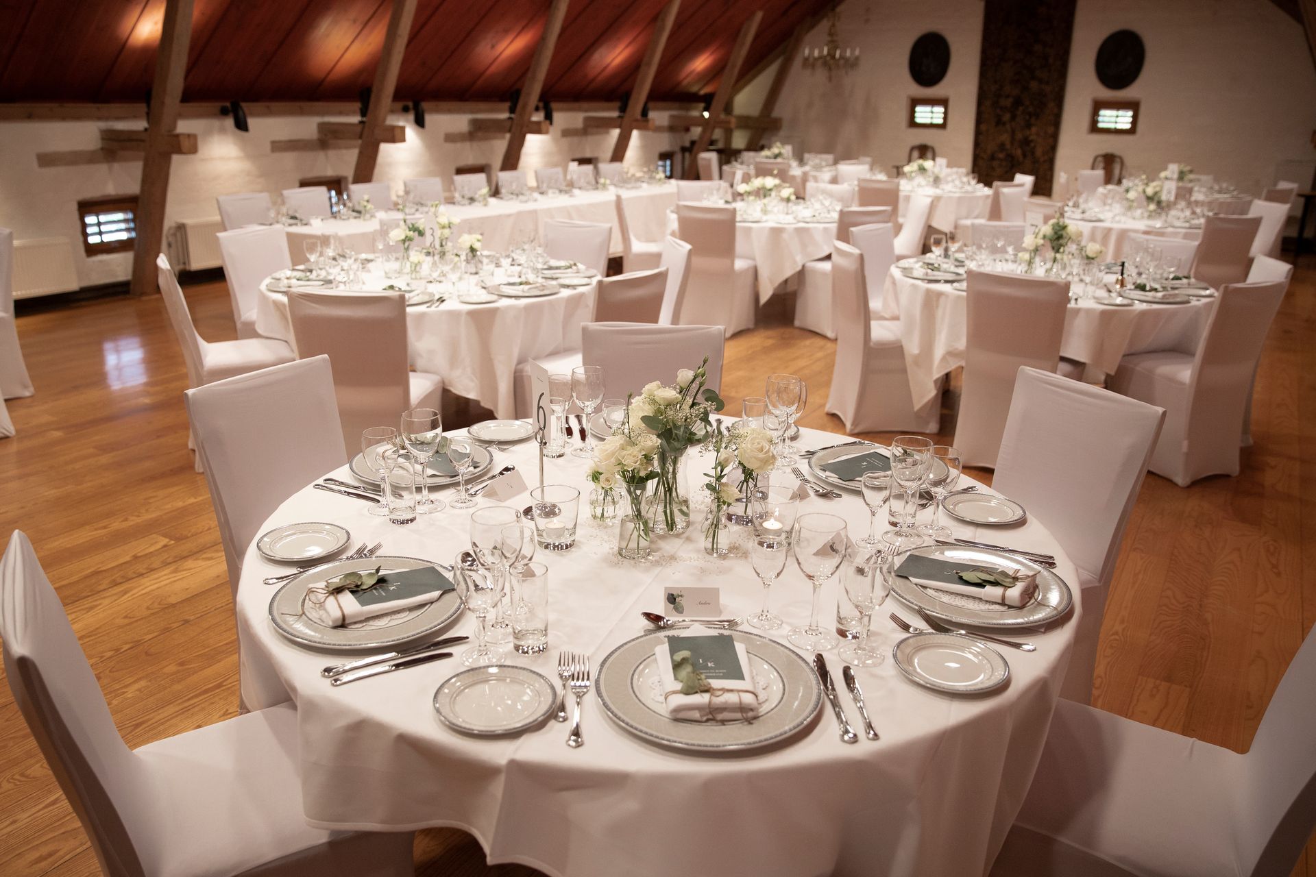 Elegant mottakelsessal med runde bord dekket for et formelt arrangement. Hvite duker og blomsterdekorasjoner.