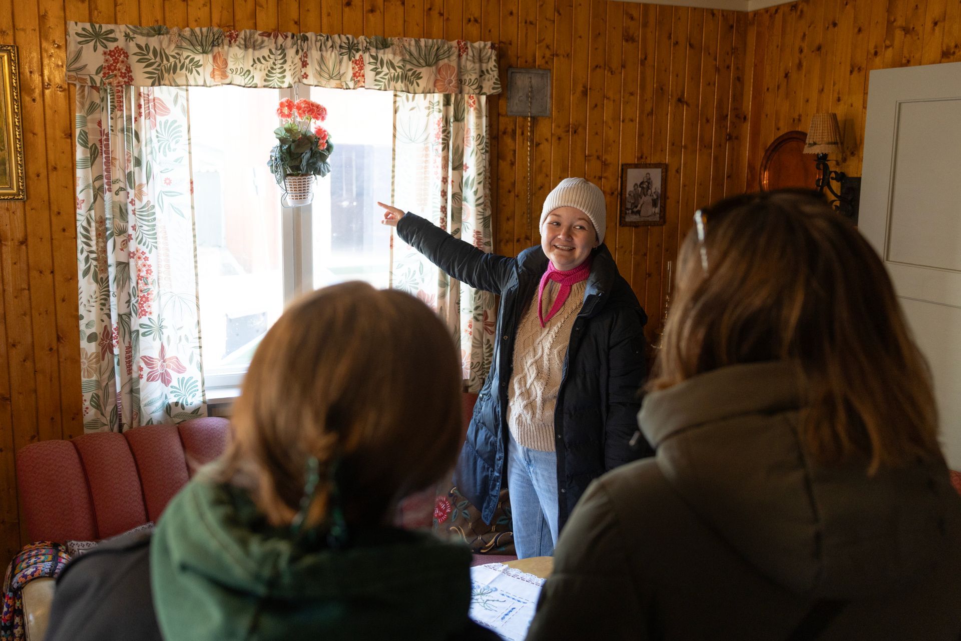En omviser peker mot vinduet og snakker med to andre i et rom med trepanel.