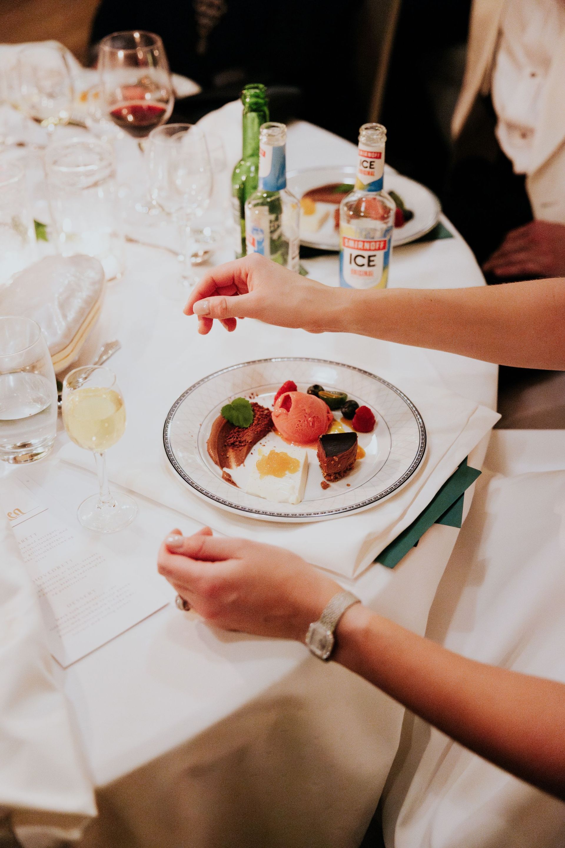 En person rekker etter en desserttallerken ved et middagsbord. Desserten inkluderer iskrem, bær og mynte.