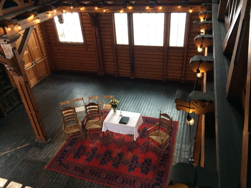 Et innendørs arrangementslokale med trevegger, et teppe, stoler og et borddekket for en seremoni.