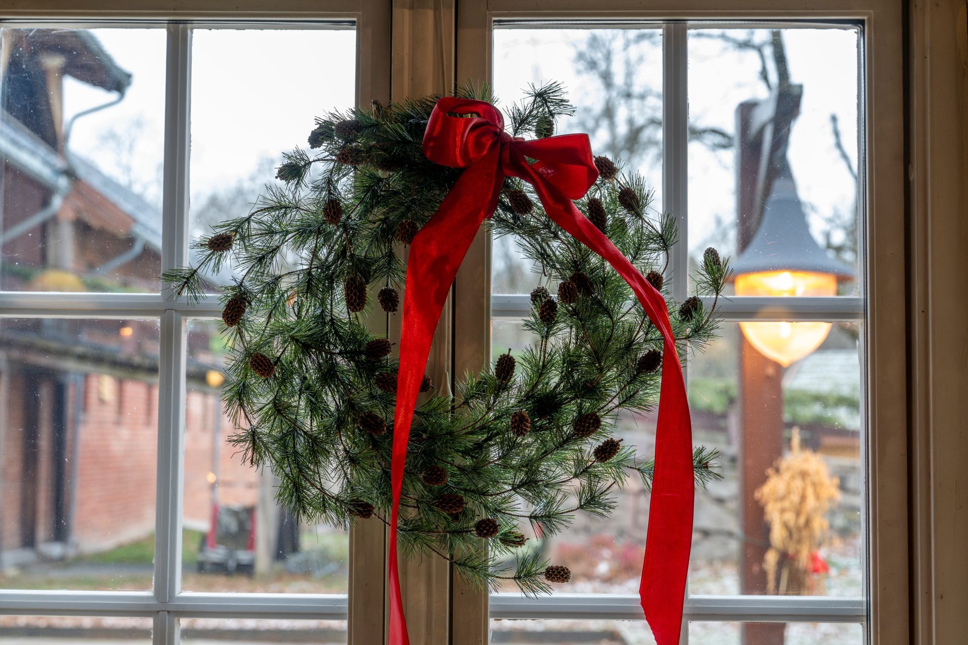 En krans med rød sløyfe henger på et vindu med et uskarpt utendørssceneri synlig.
