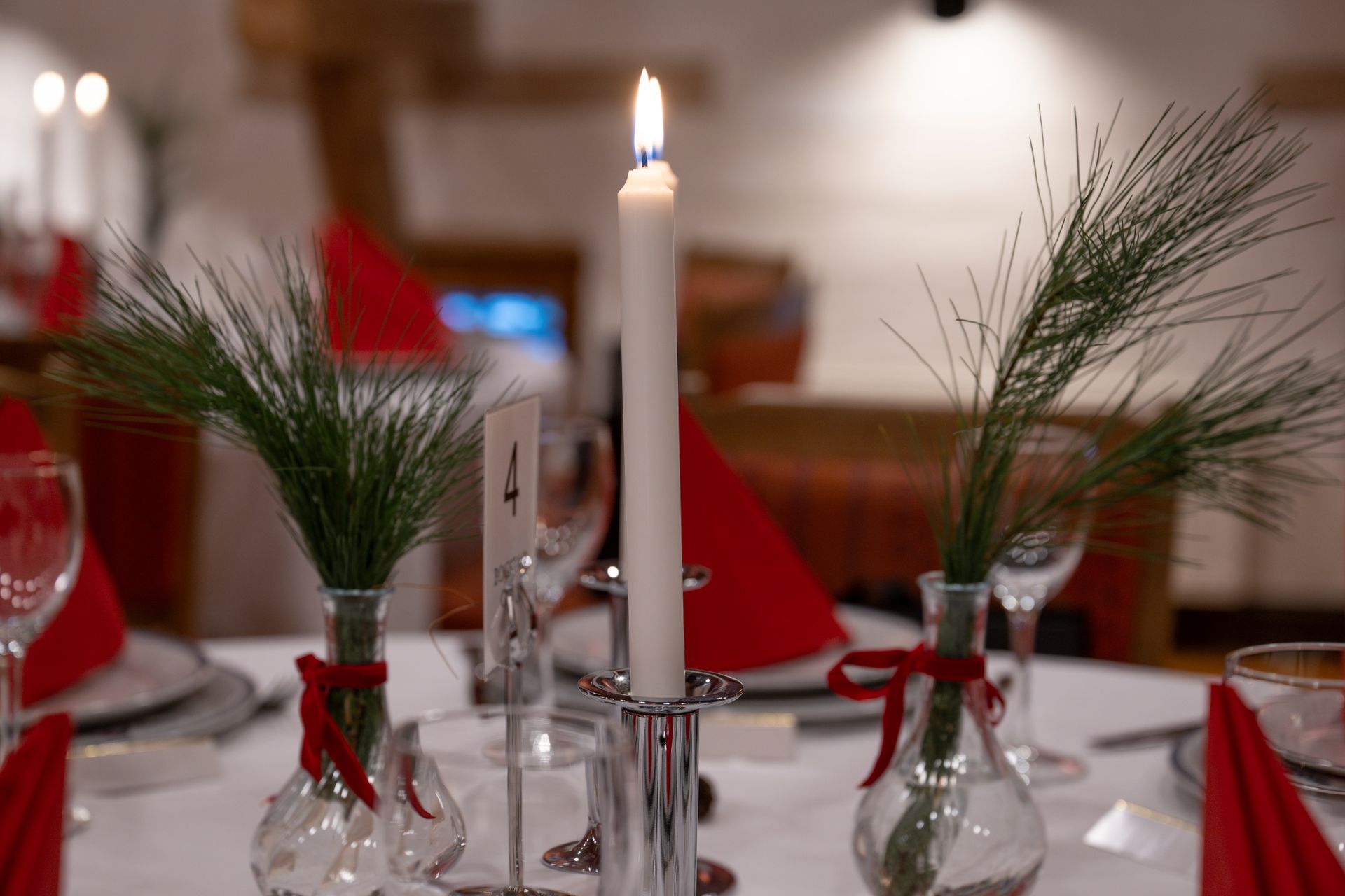 Borddekking med tente lys, grønt i vaser og røde servietter.
