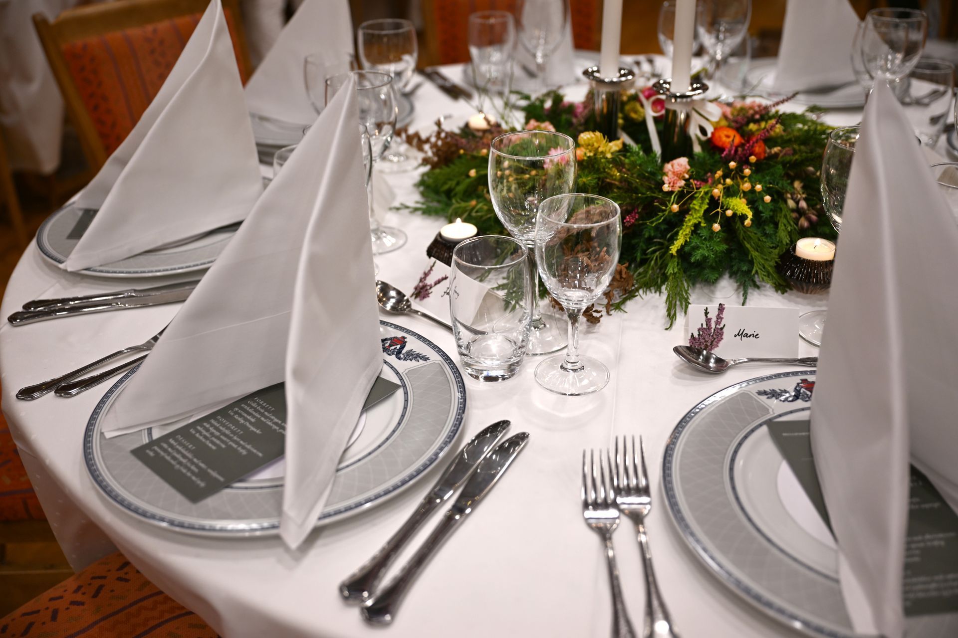 Formell borddekking med hvitt sengetøy, sølvtøy og midtpunkt.