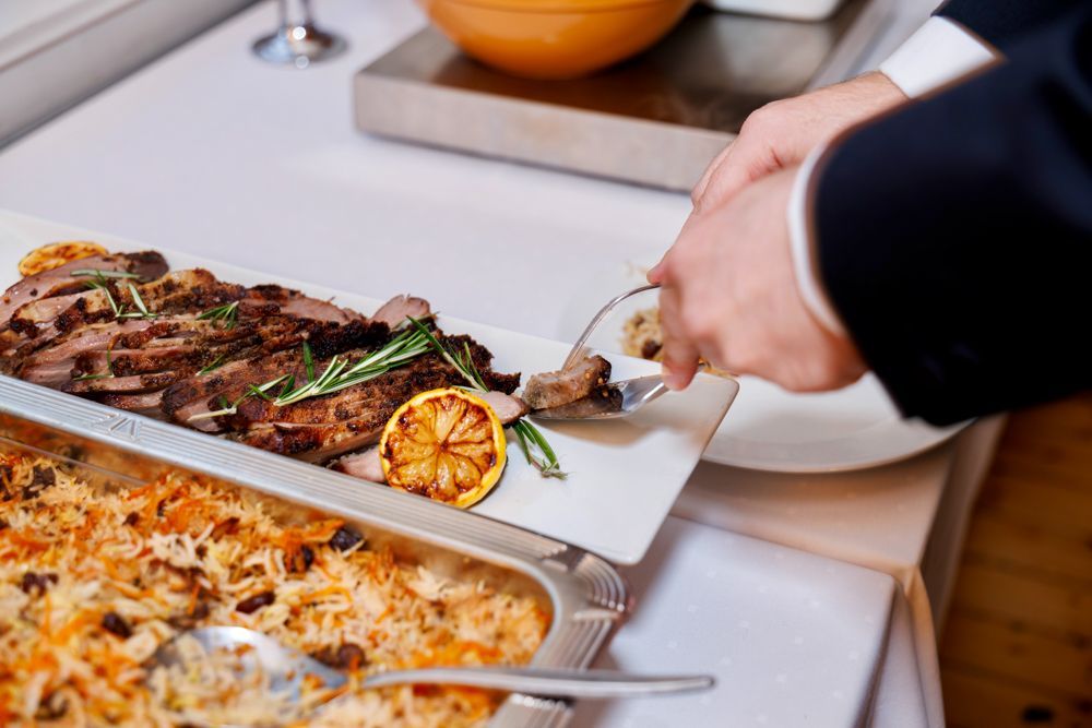 En mann forsyner seg av  stekt kjøtt fra et fat på en tallerken ved en buffé.