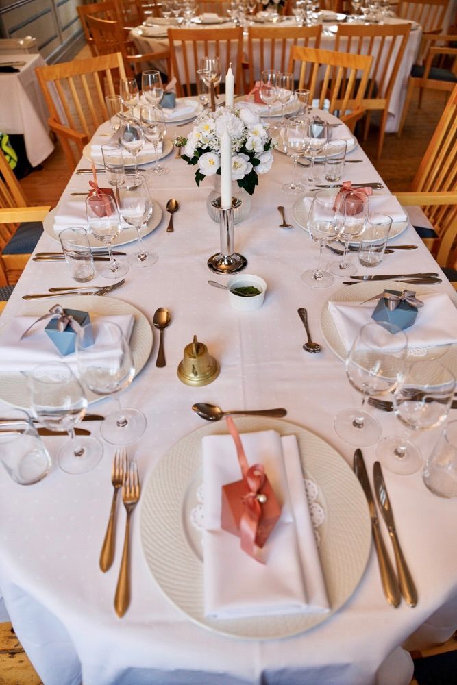 Formell borddekking med hvit duk, sølvtøy, glass og et blomsterdekorasjon på midten.