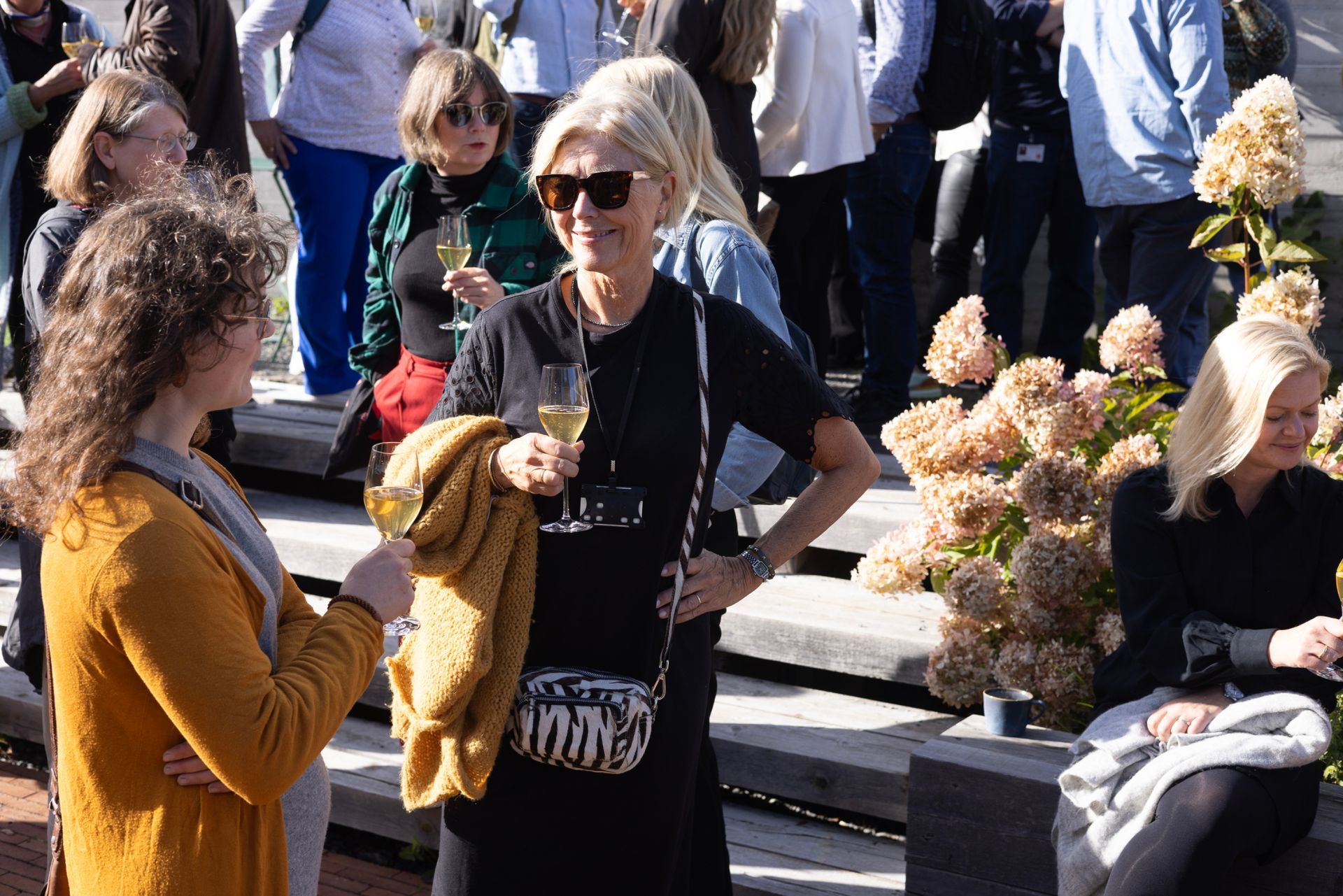 Langt trebord dekket for et måltid inne i et drivhus, omgitt av planter og sollys.