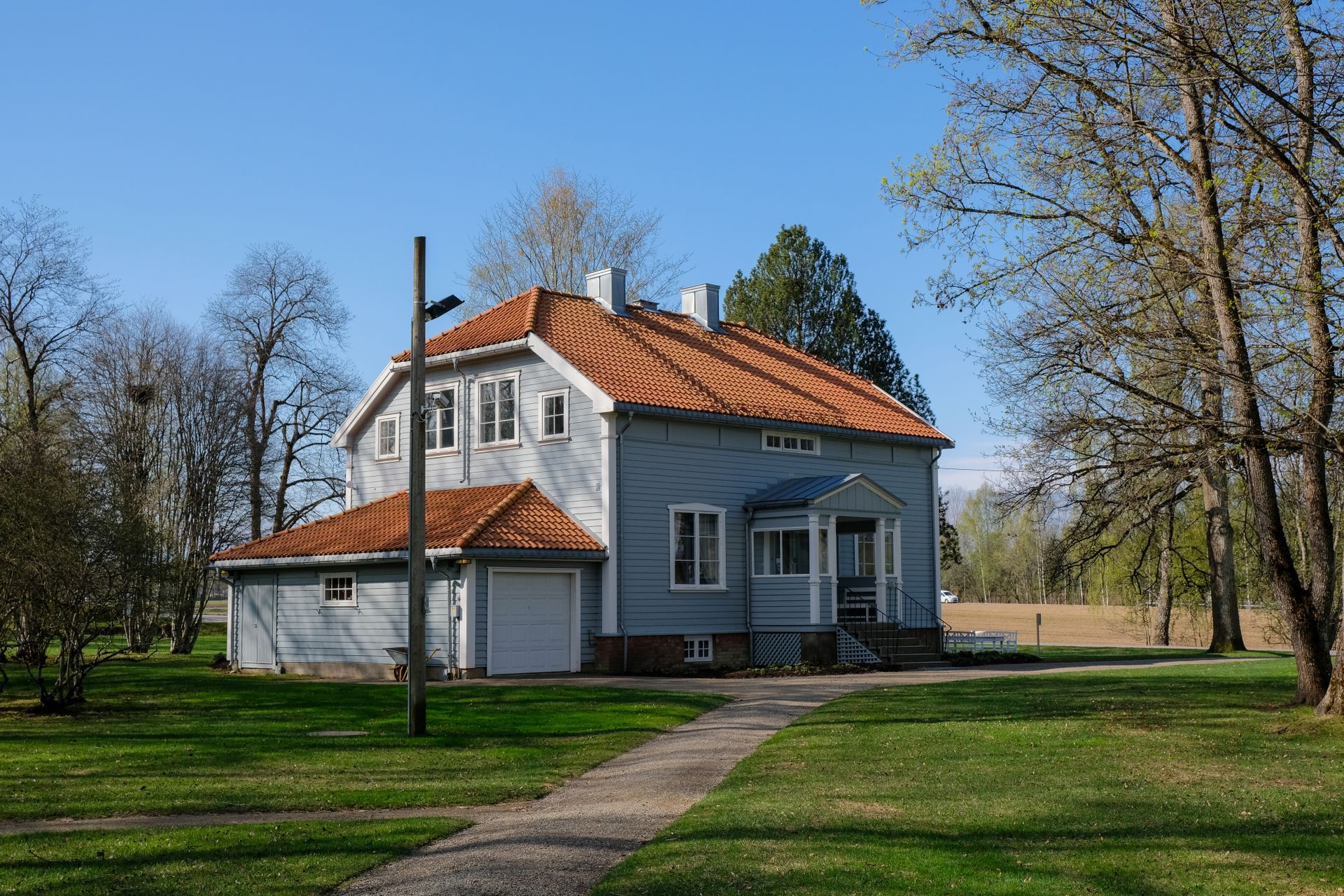 Blått hus med oransje tak, garasje og gangvei på grønn plen, under en blå himmel.