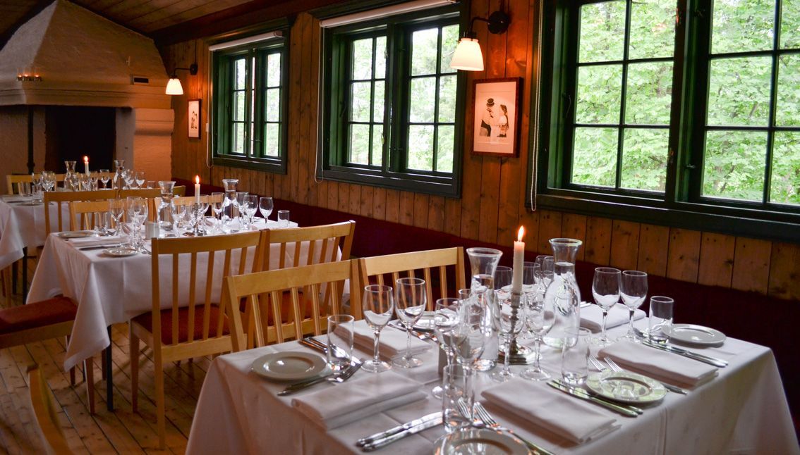 Spisesal med dekkede bord for gjester; trevegger, grønne vinduer og levende lys.