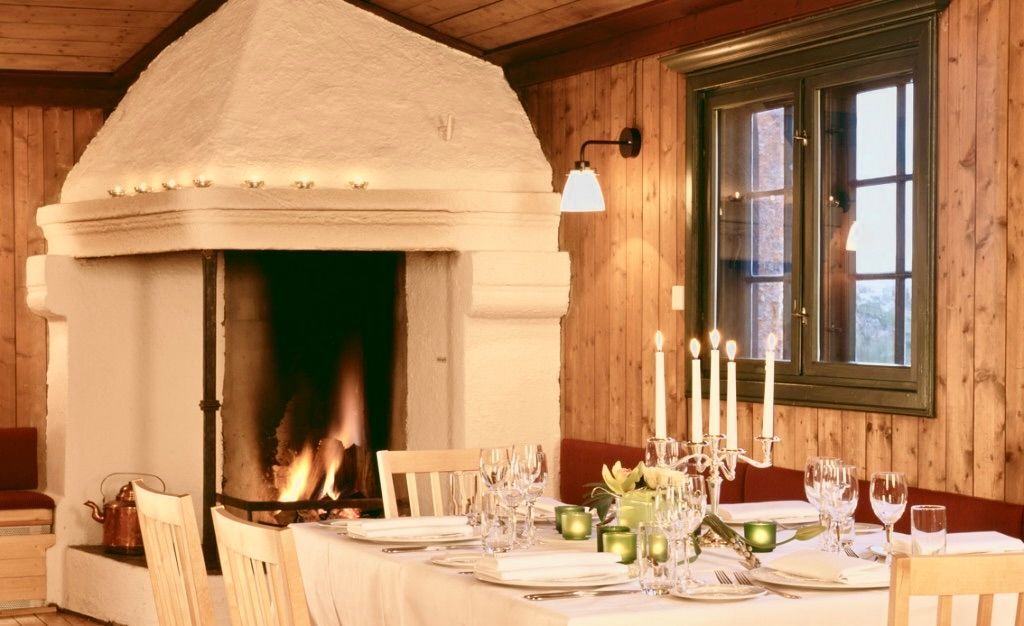 Koselig spisestue med tent peis, dekket bord for måltider, trevegger og vindu.