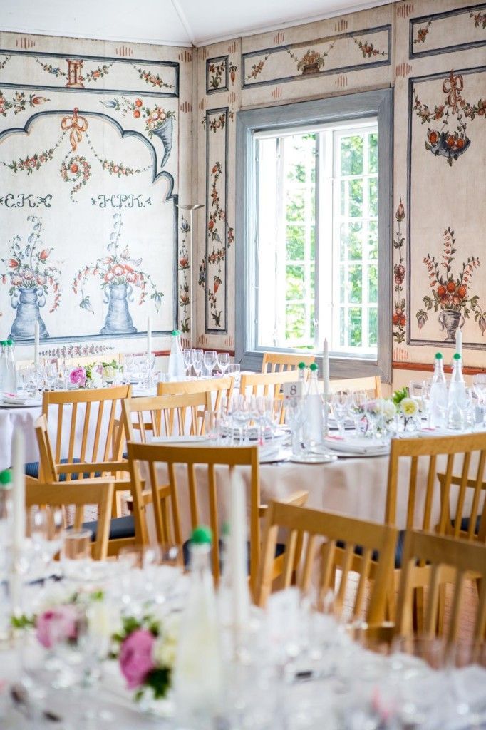 Spisestue med blomstermalte vegger, trestoler og et vindu med utsikt over grøntområder.