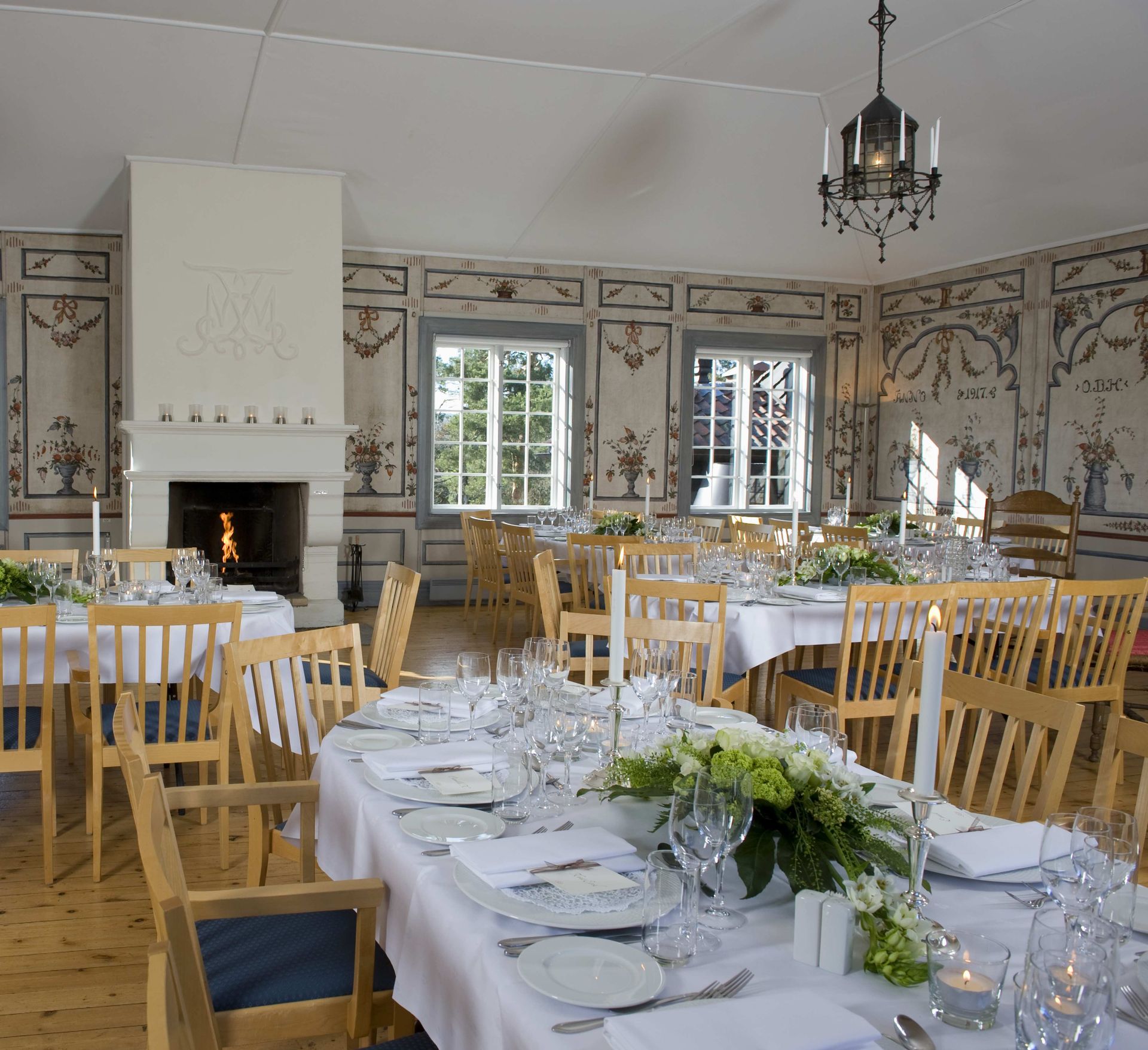 Elegant spisestue med dekkede bord til måltider, peis og utsmykkede veggdekorasjoner.