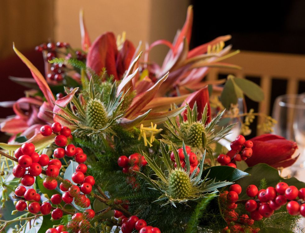 Nærbilde av et blomsterarrangement med røde bær, tistler og rosa liljer.