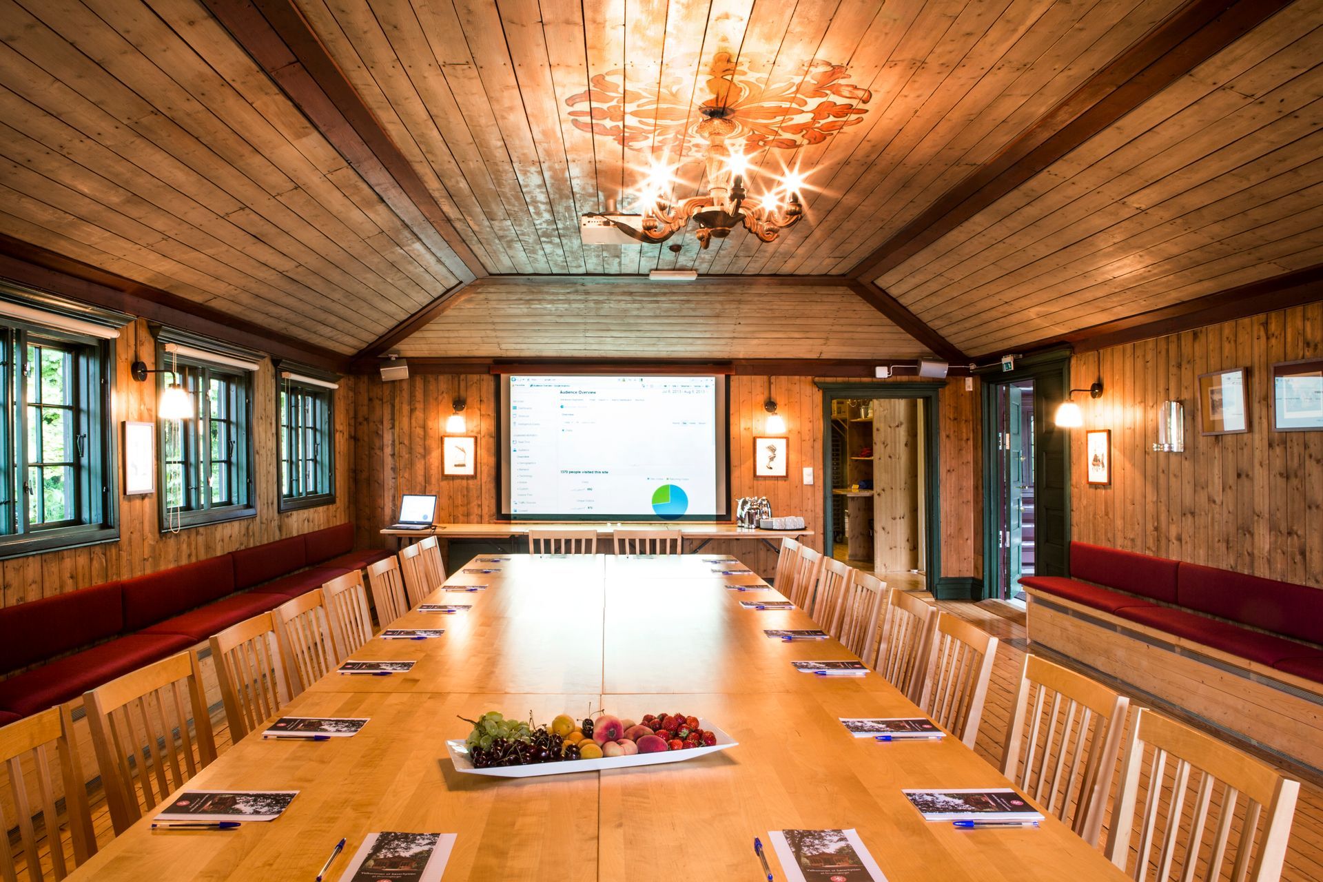 Konferanserom med et langt trebord, projektorlerret og trepanel.