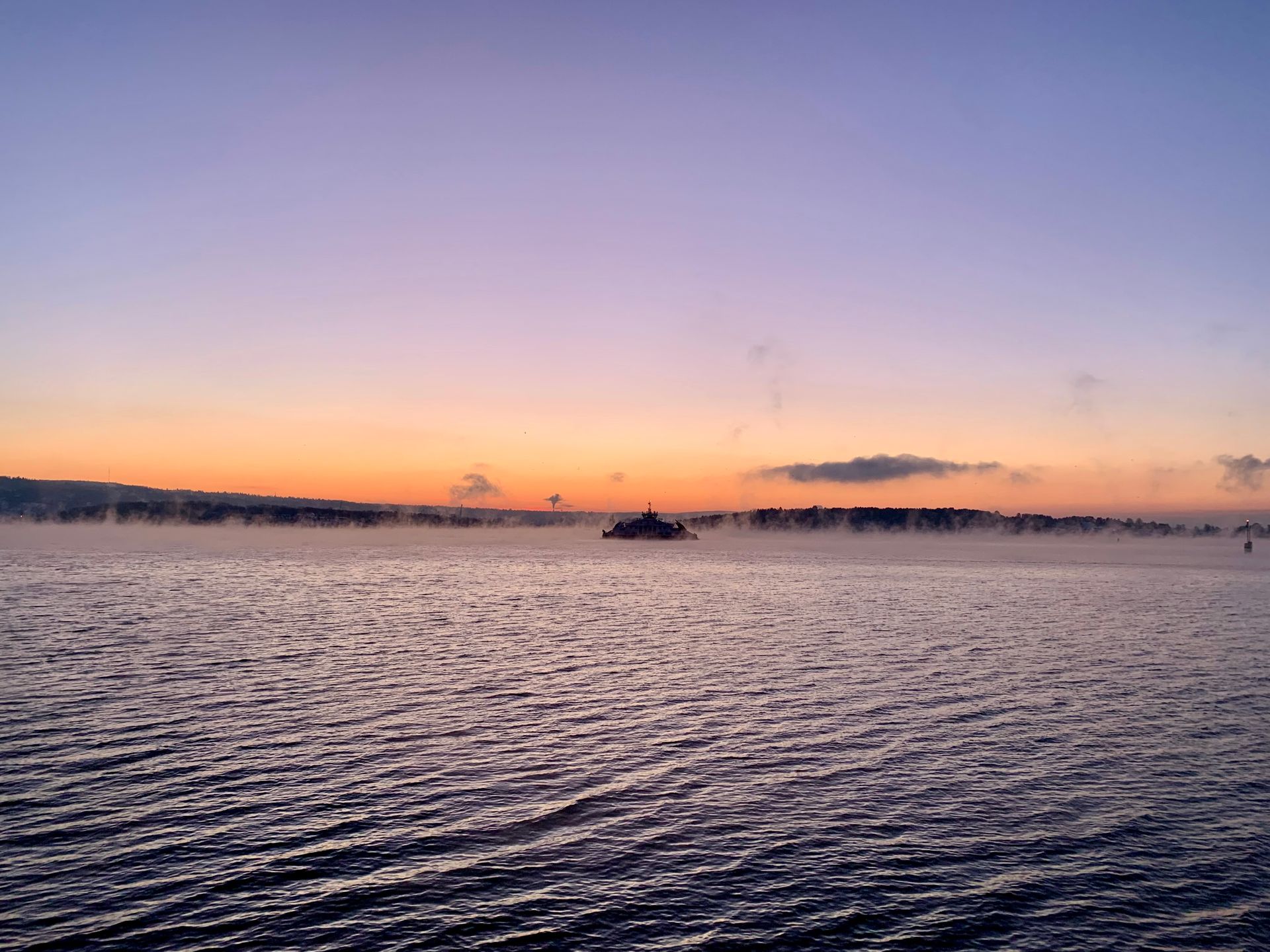Solnedgang over et vann med en disig horisontlinje, oransje og lilla himmel.