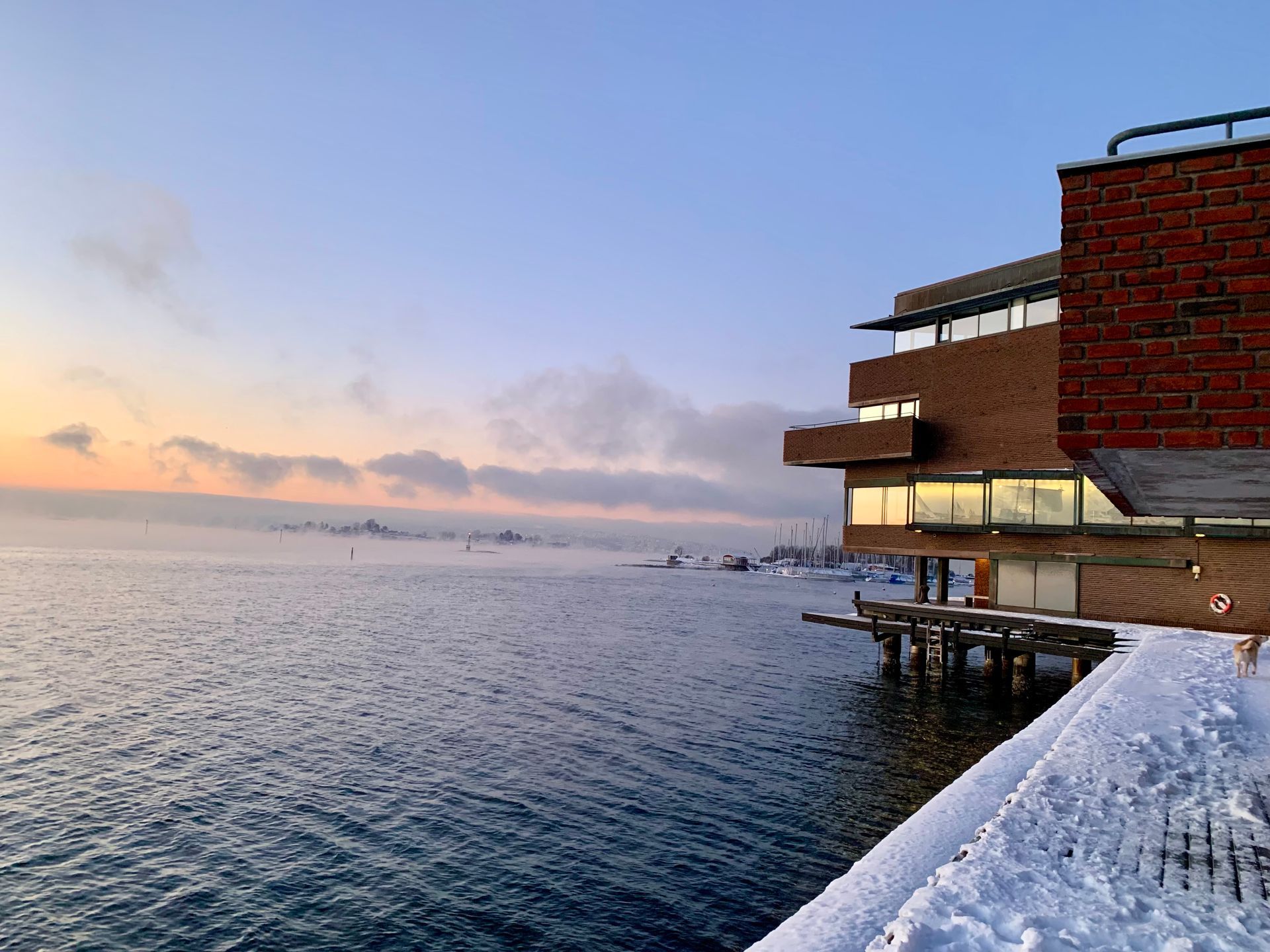 Norsk Maritimt Museum ligger ved en snødekt brygge, og har utsikt over rolig vann, med en soloppgang i bakgrunnen. Dette bilde er en lenke til Norsk Maritimt Museum