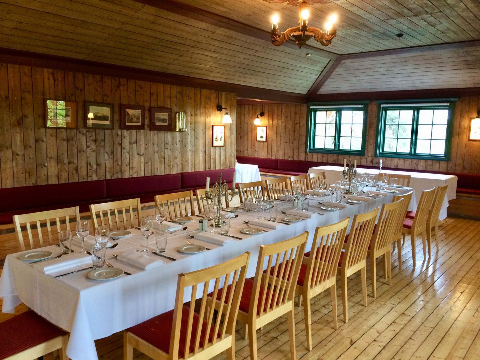 Langt spisebordsett til et formelt arrangement i et rustikt rom med trevegger og grønne vinduer.