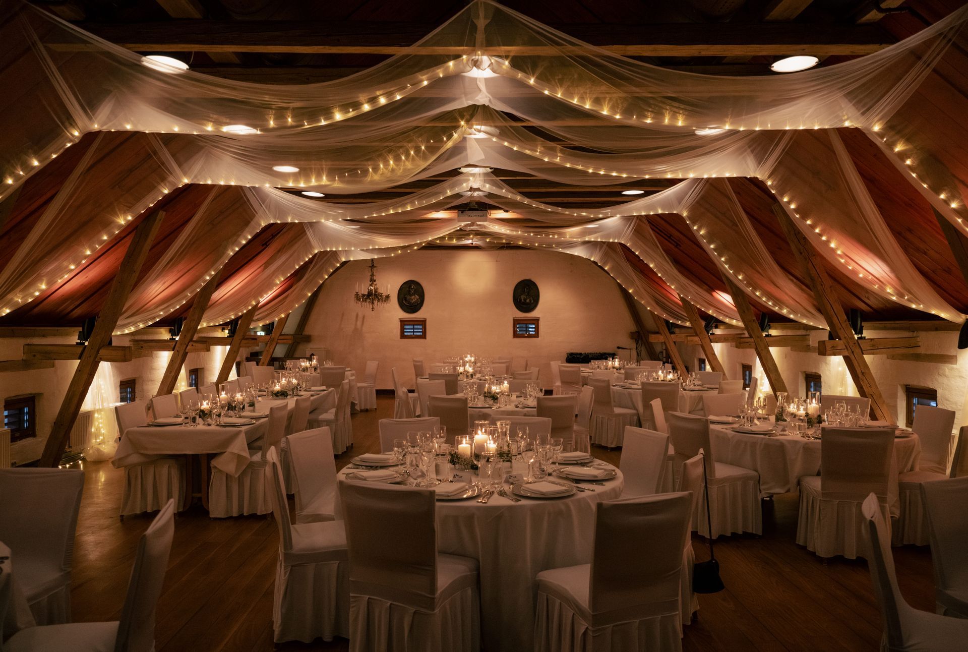 Elegant banquet hall with white-clothed tables, warm draped lighting, and twinkling ceiling lights