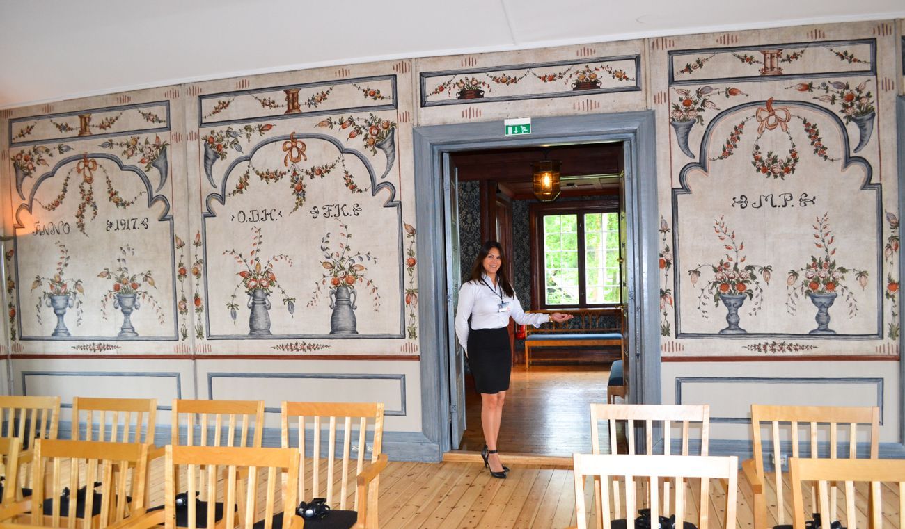 Kvinne står i døråpningen til et rom med malte vegger og stoler.