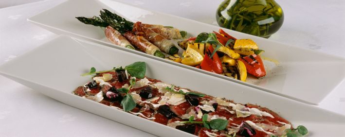 To rektangulære tallerkener med mat: asparges med kjøtt, grillet paprika og en rød rett med oliven og ost.