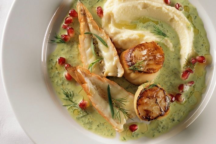 Sjømatrett med stekte kamskjell, fylte reker, potetmos og grønn saus, garnert med granateplekjerner.