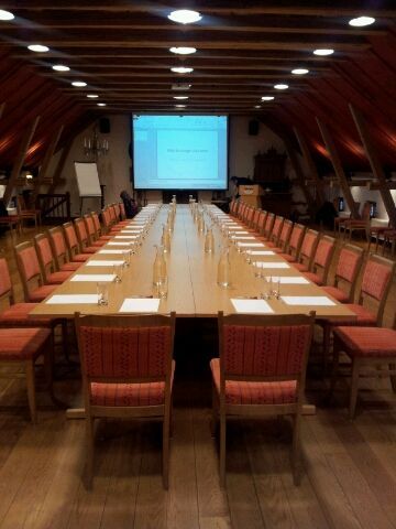 Langt konferansebordsett for et møte i et rom med trepanel, med en skjerm i den ene enden.