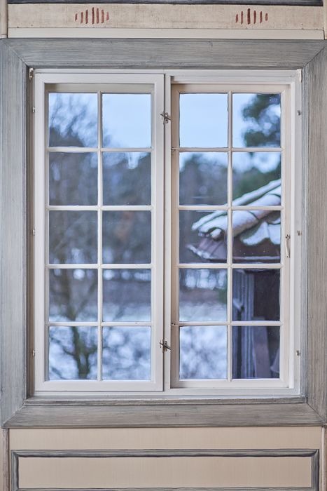 Todelt vindu med hvitt rutenett, med utsikt over et snøhvit, uskarpt utendørsscene. Kremfargede og grå lister.