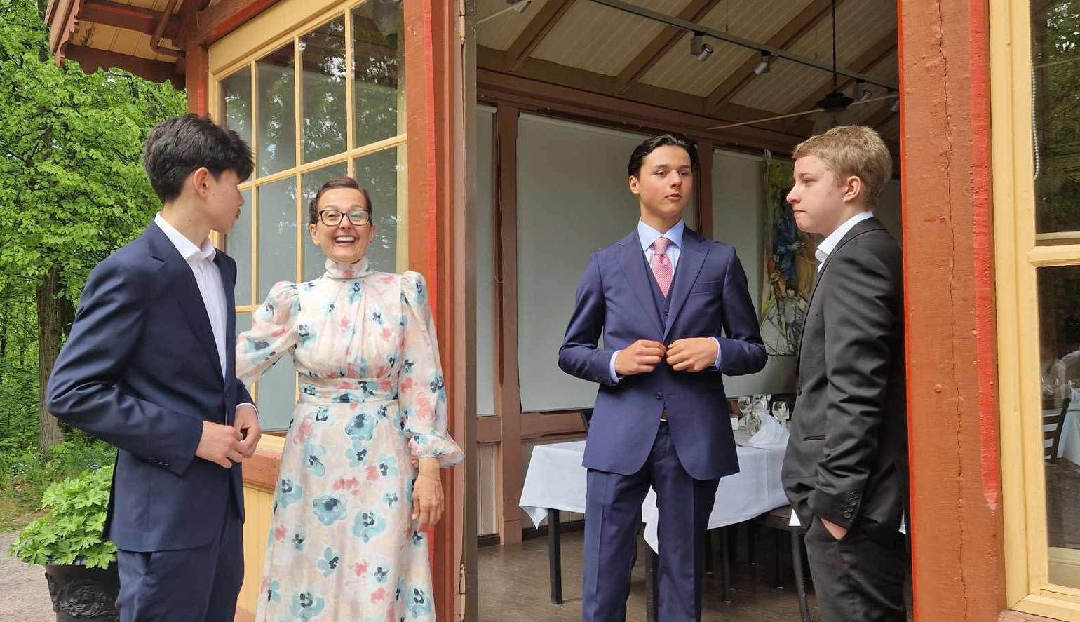 Fire personer i formelle antrekk står utenfor en bygning. Én kvinne smiler, de andre har på seg dress.