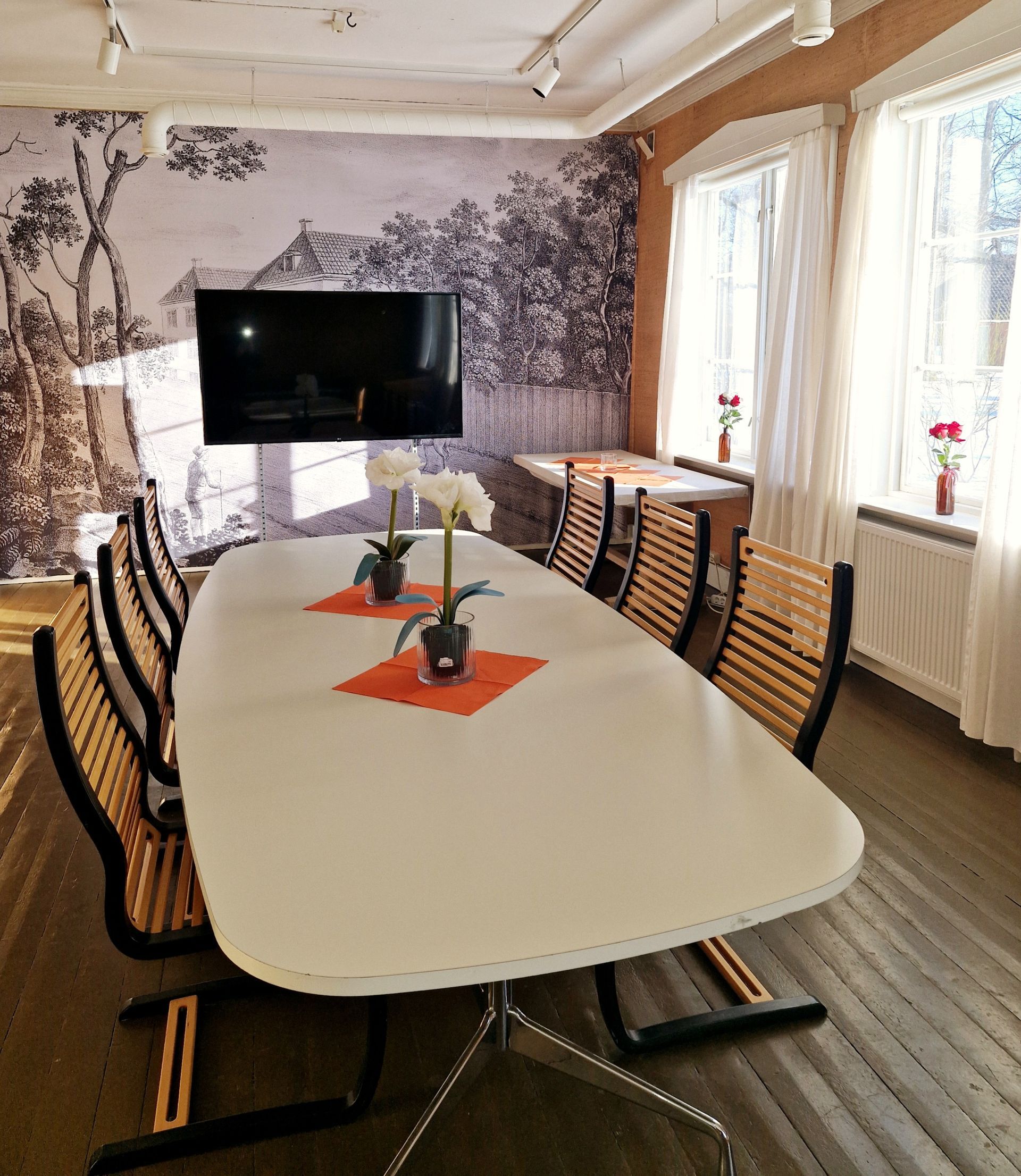 Konferanserom med stort hvitt bord, stoler, TV og tapet.