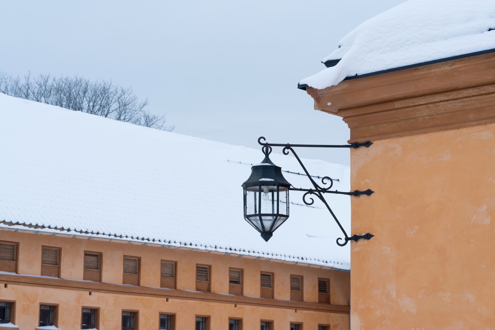 Snødekt bygningseksemplar med utsmykket svart lampe. Beige vegger og tak, overskyet himmel.