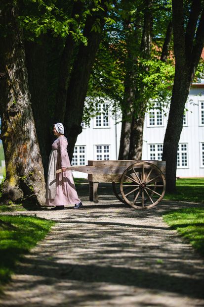 Omviser som går med gammeldags kjerre i en grønn allé. 