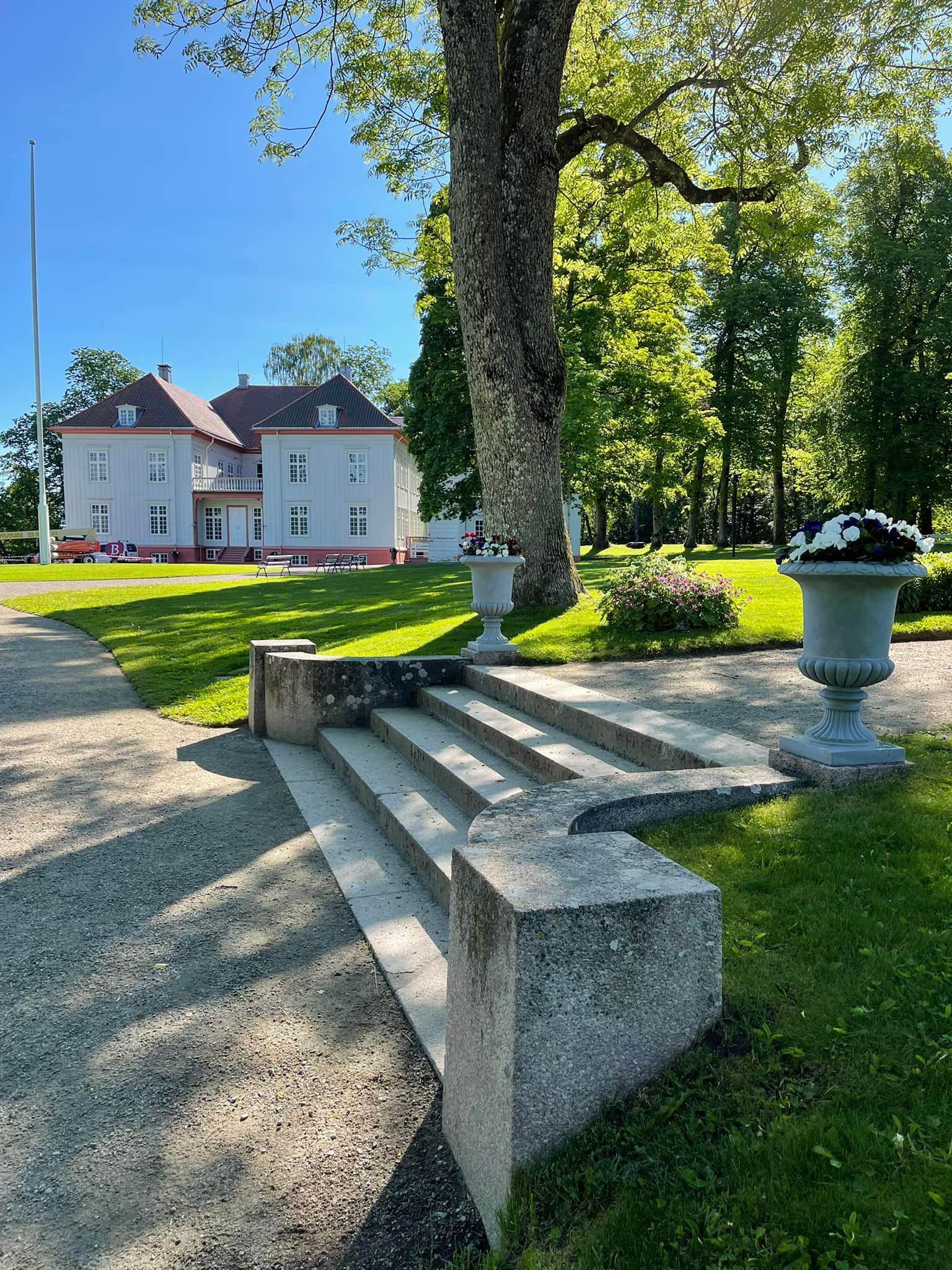 Steintrapper fører til en lys bygning med rødt tak, på en solrik, grønn plen.