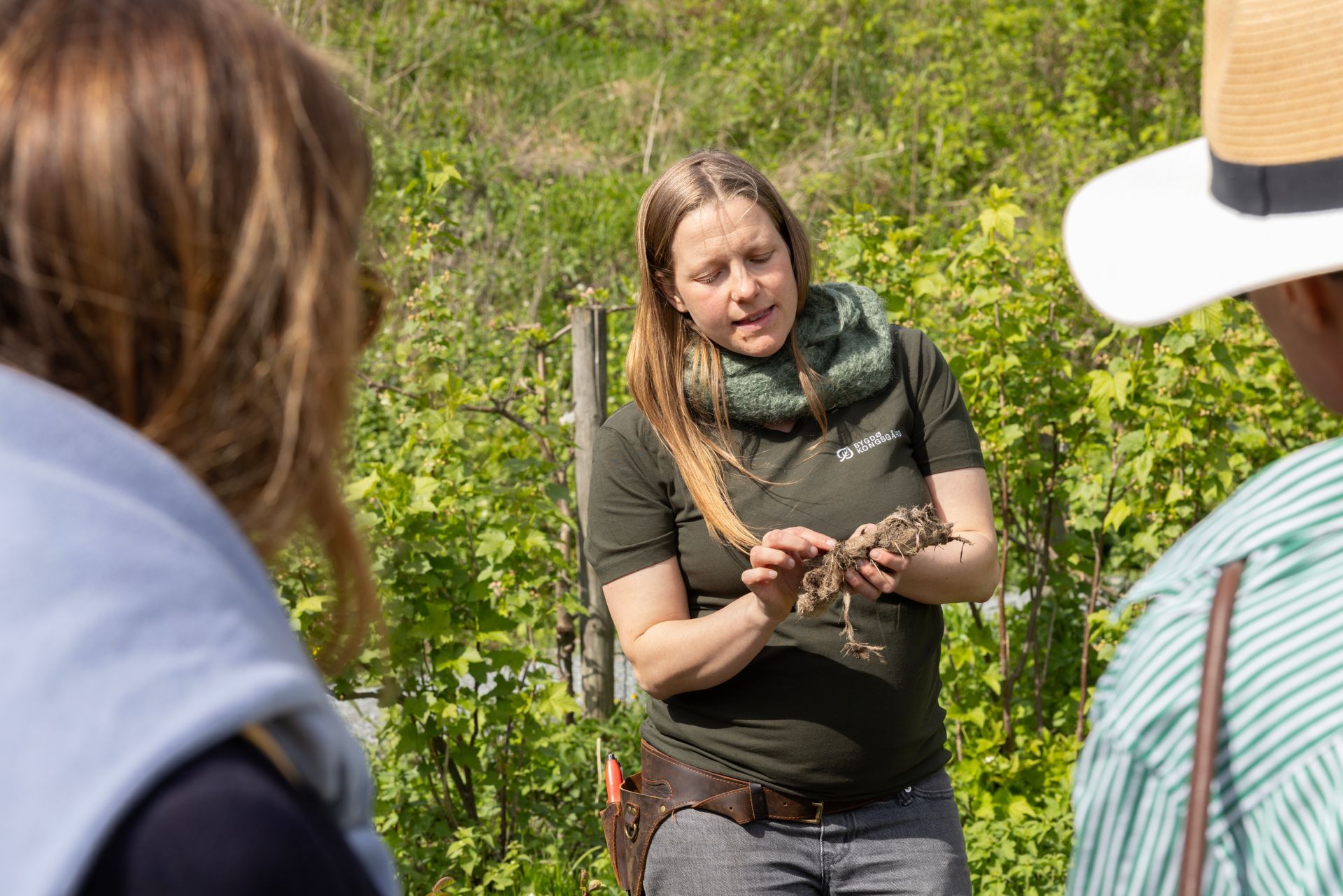 Kvinne i grønn skjorte forklarer noe, holder en fugl, utendørs.