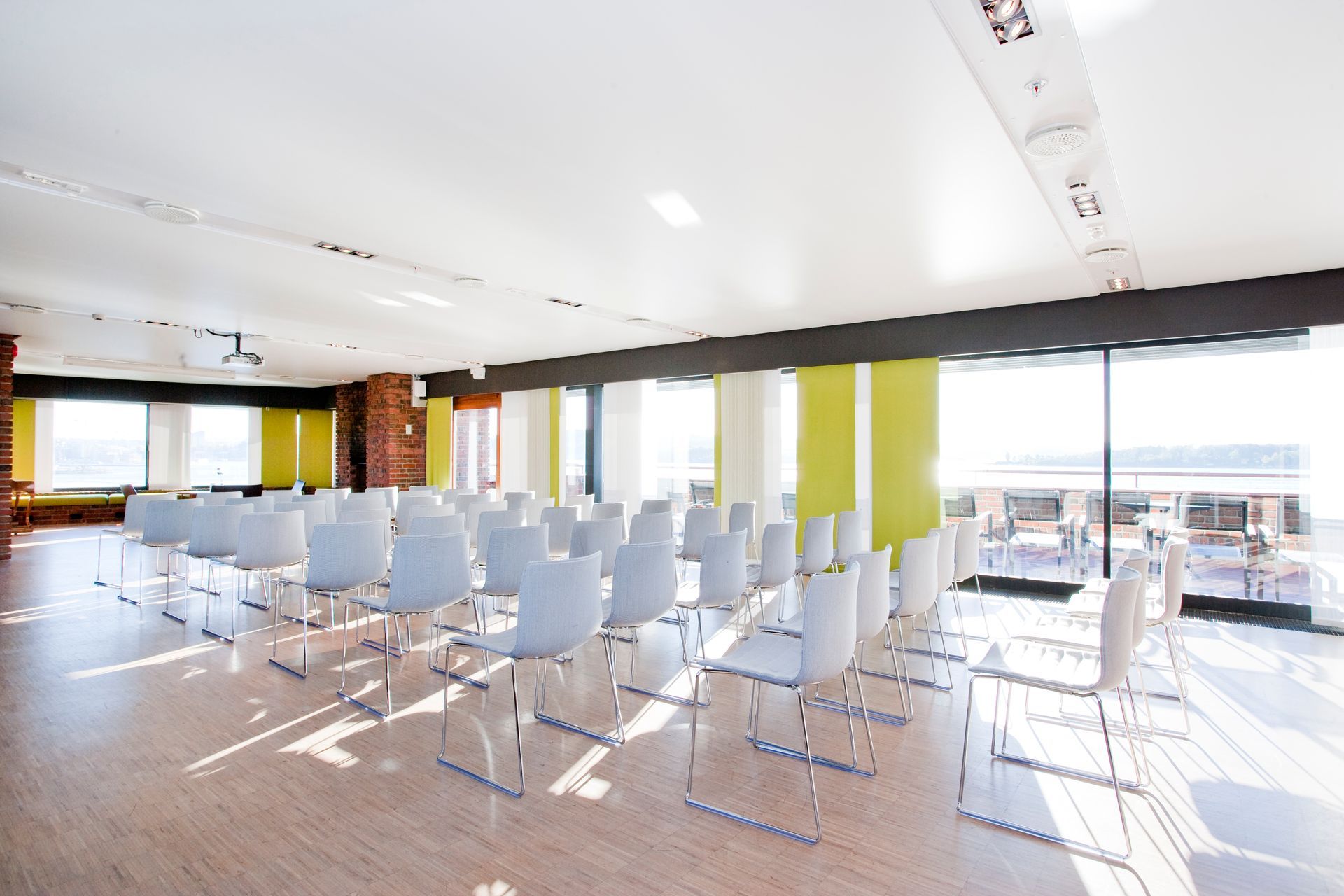 Konferanserom med rader med hvite stoler, store vinduer og sterk belysning.