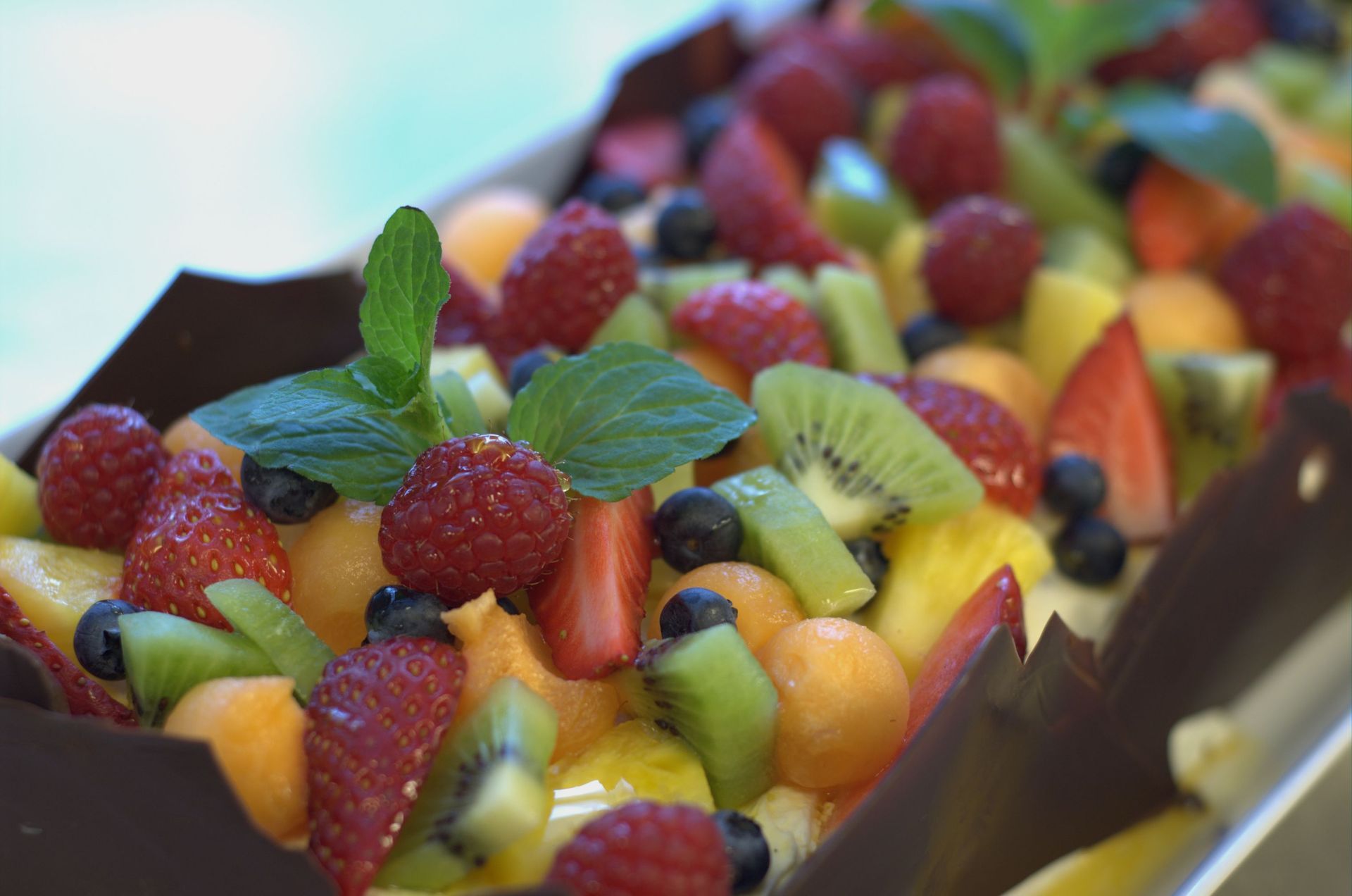 Fruktterte med bringebær, jordbær, kiwi, blåbær, cantaloupemelon og ananas, dekorert med mynte.