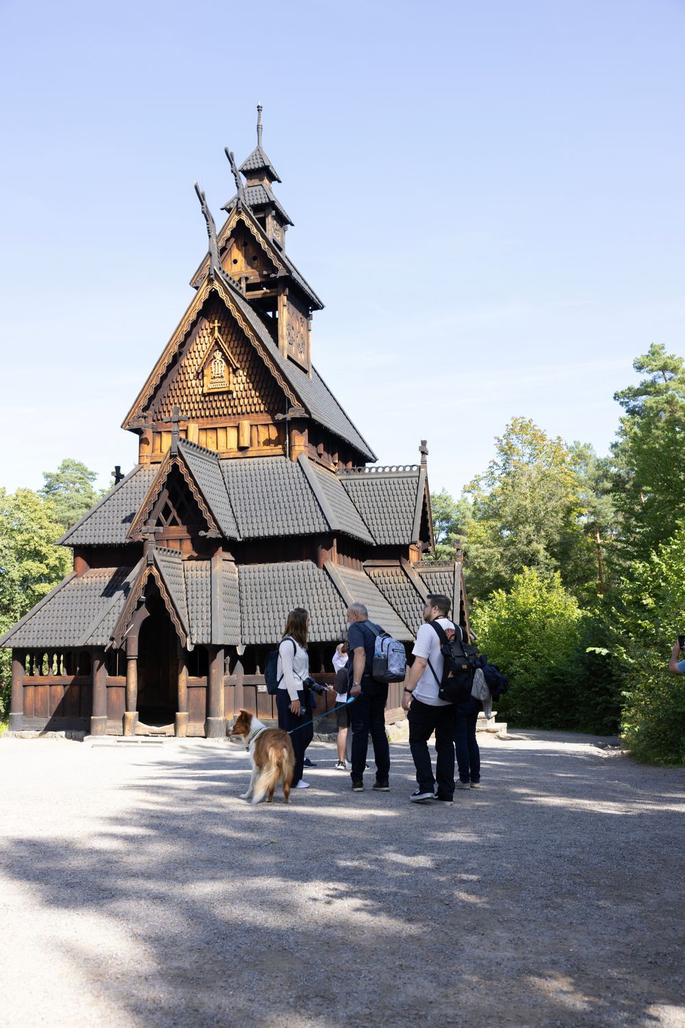 Stavkirke i tre med folk foran på en solskinnsdag.