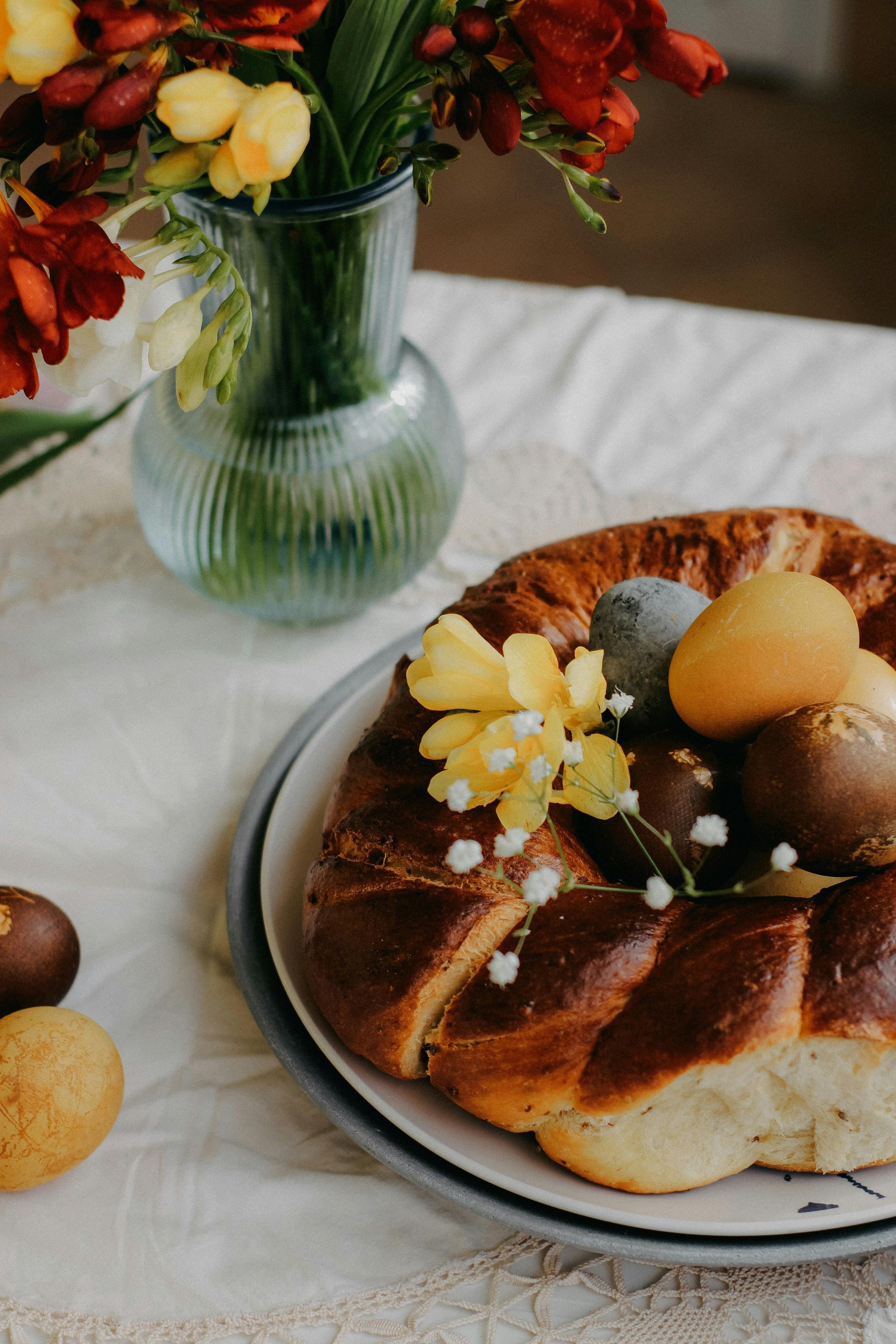 Påskebrødkrans med fargede egg og blomster på et bord.