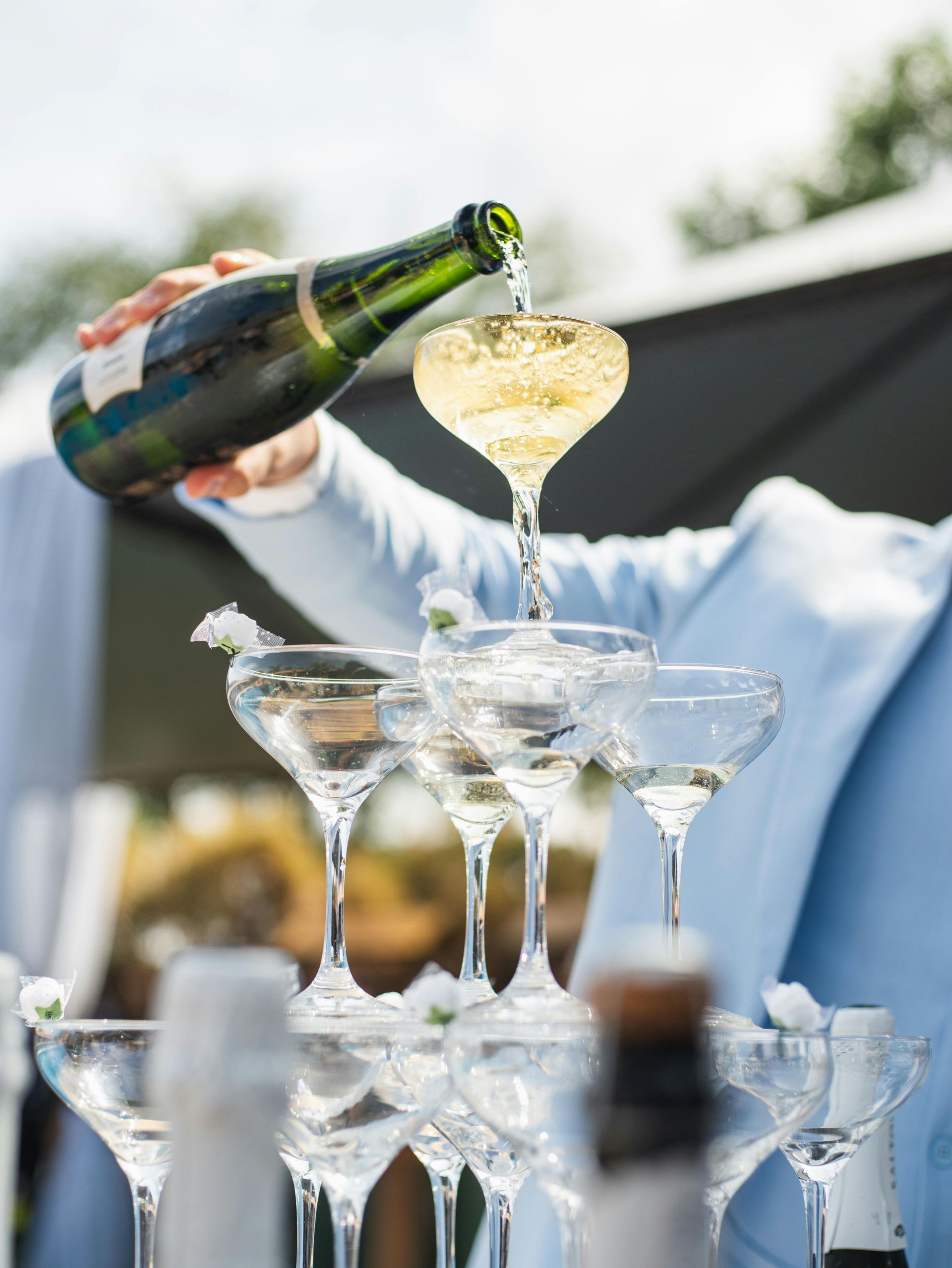 Person som heller champagne i glass stablet i et tårn på et utendørsarrangement.