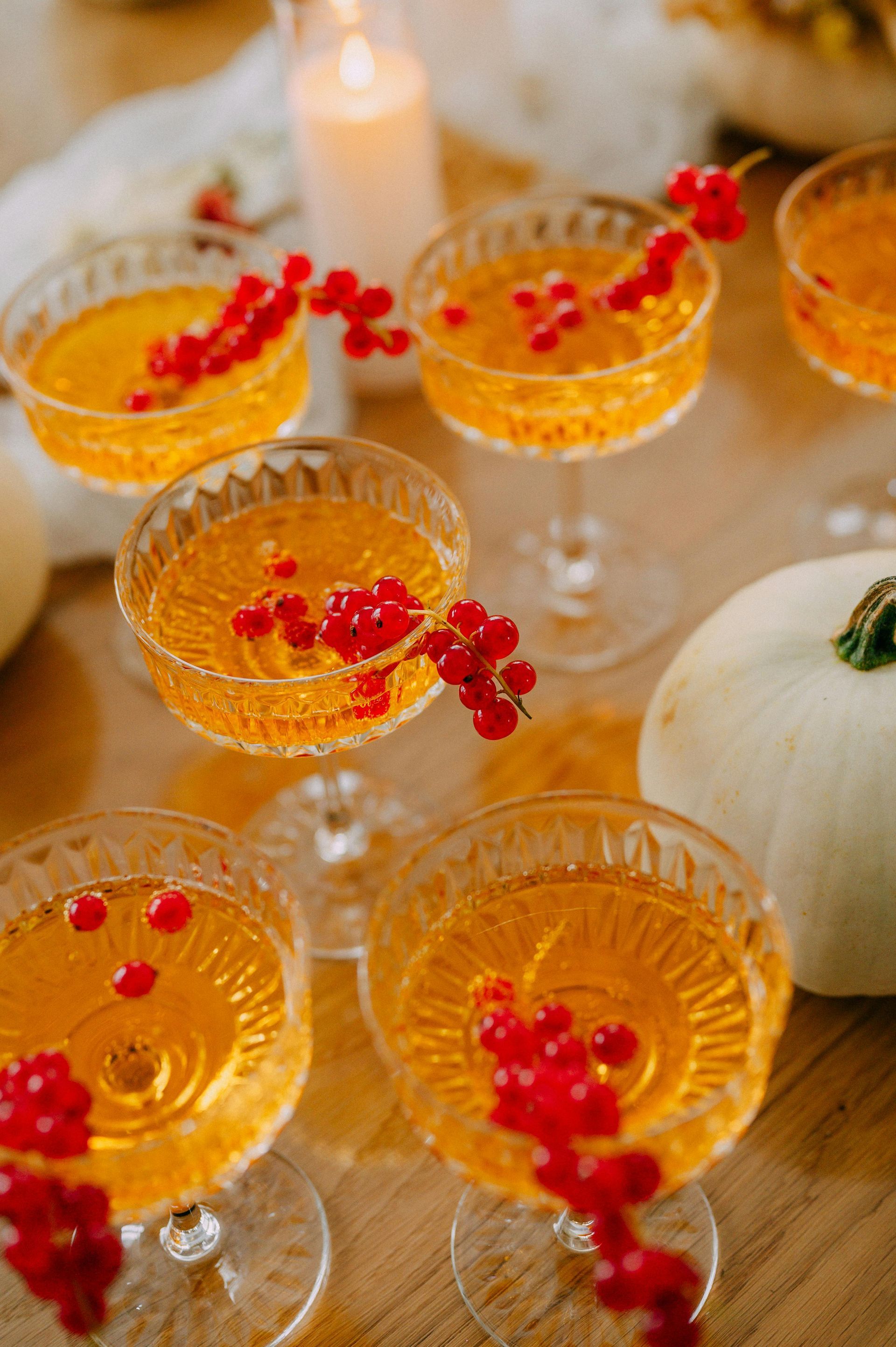 Cocktailer i glass med stilk, garnert med røde bær, på et bord.